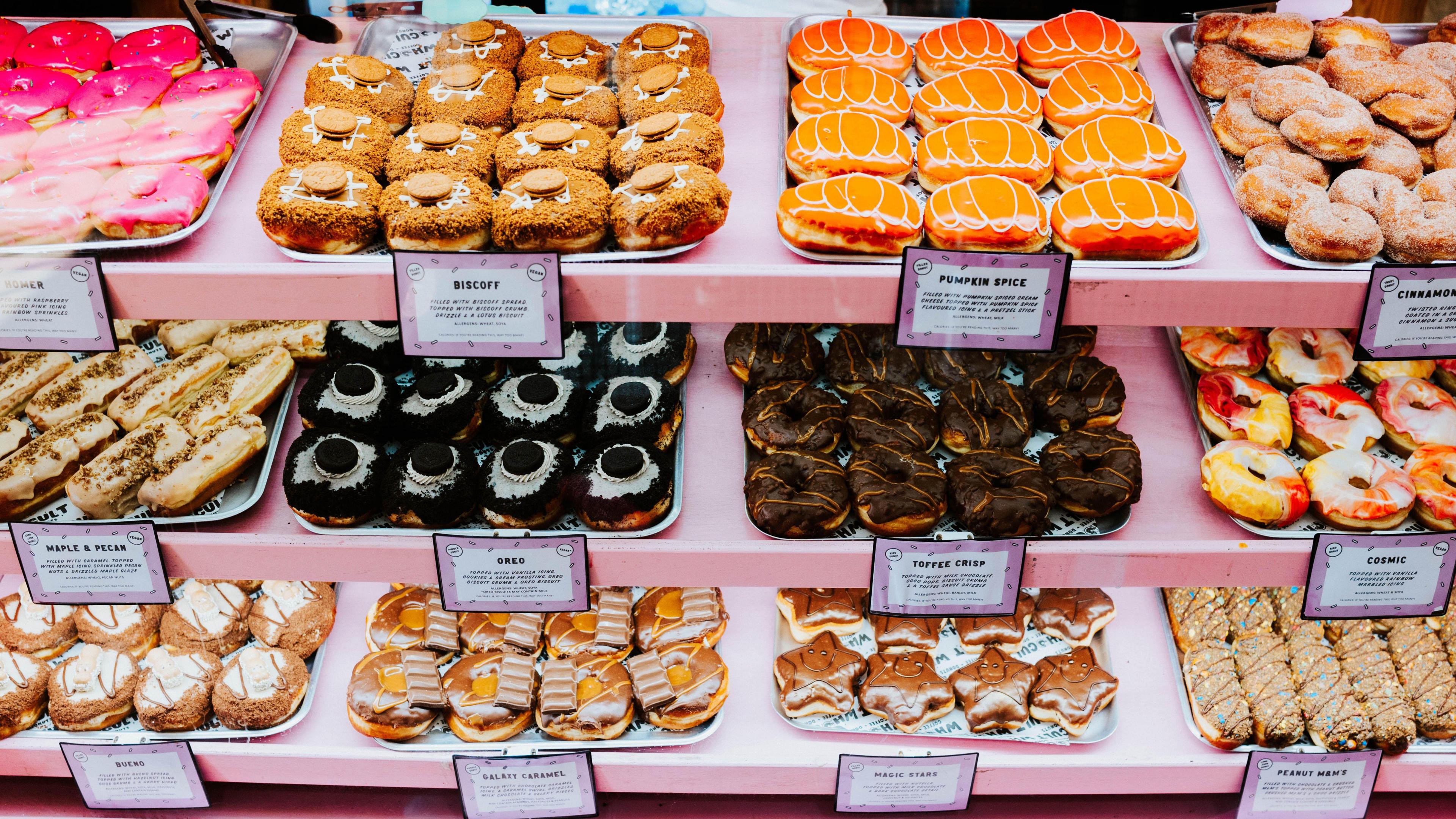 A variety of donuts can be seen in a pink display cabinet. They are particularly eye-catching with flavours ranging from Oreo to Pumpkin Spice