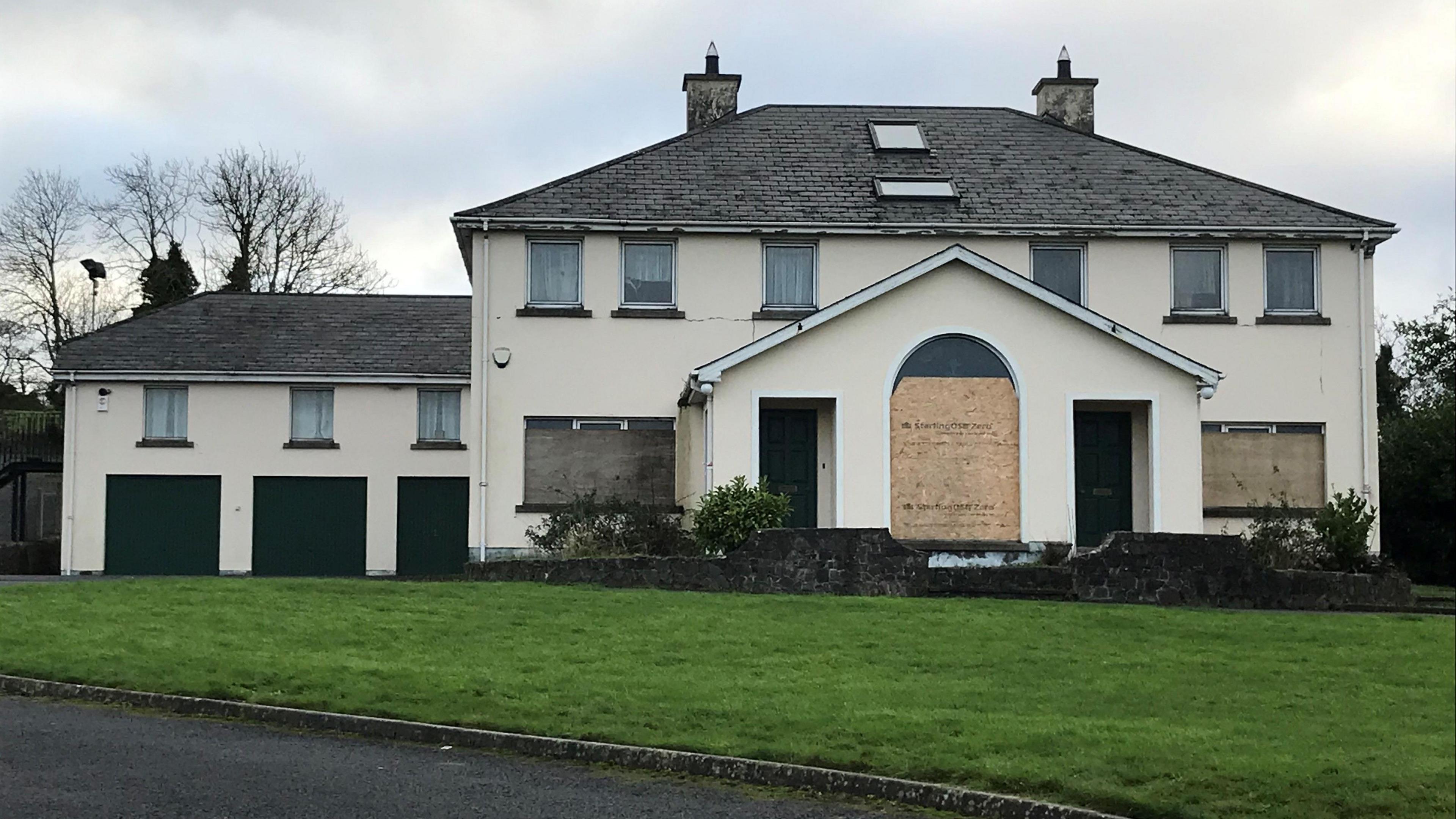 Parochial house in Hilltown. It's a large house with separate building to the left and a large porch area with two windows boarded up.
