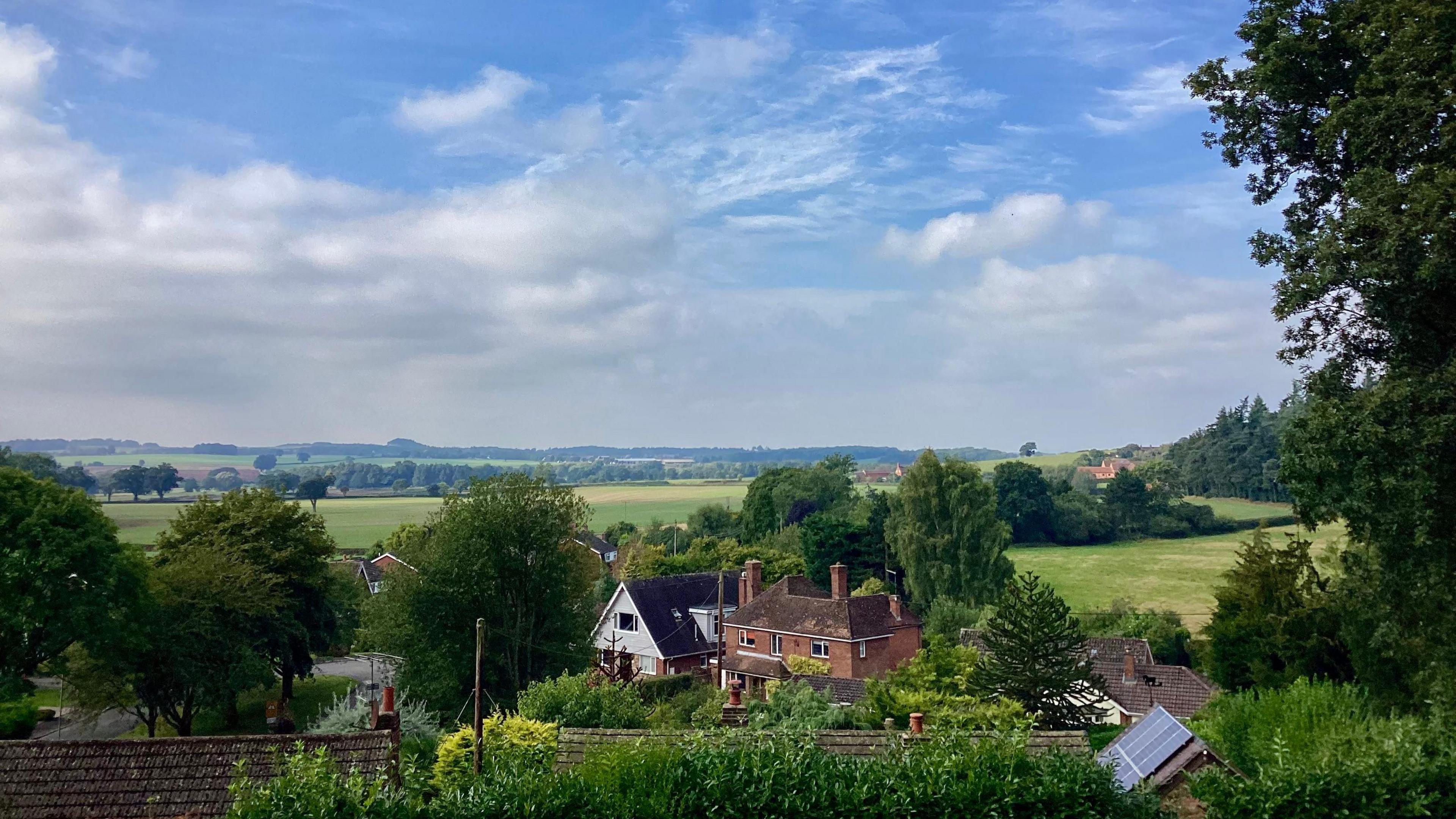 A view over the roofs of houses in Great Chatwell, Staffordshire, showing a cloudy, blue sky.