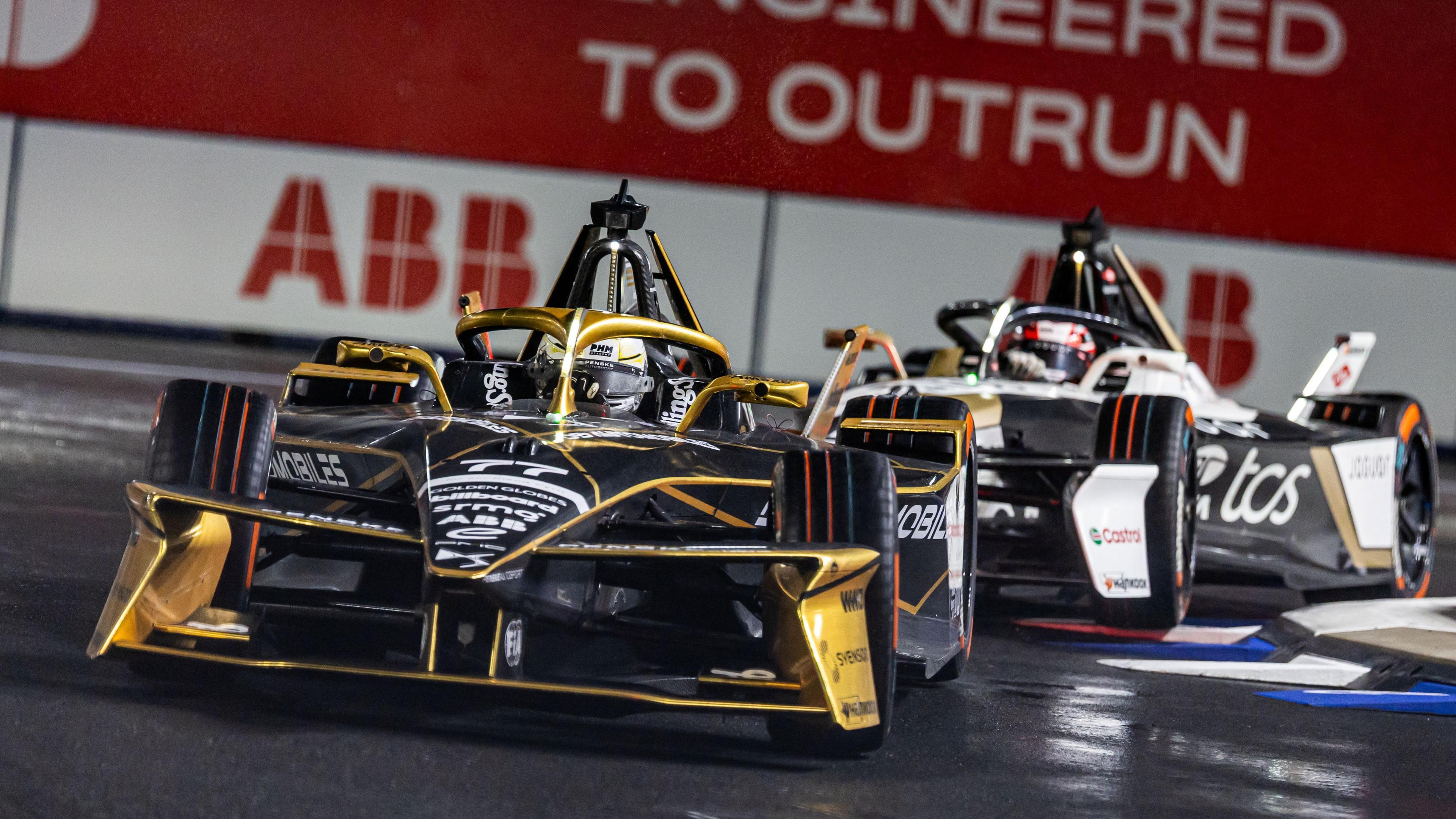 Taylor Barnard drives in a black Formula E sports car with gold trim. There is another car chasing behind him which is black and white.