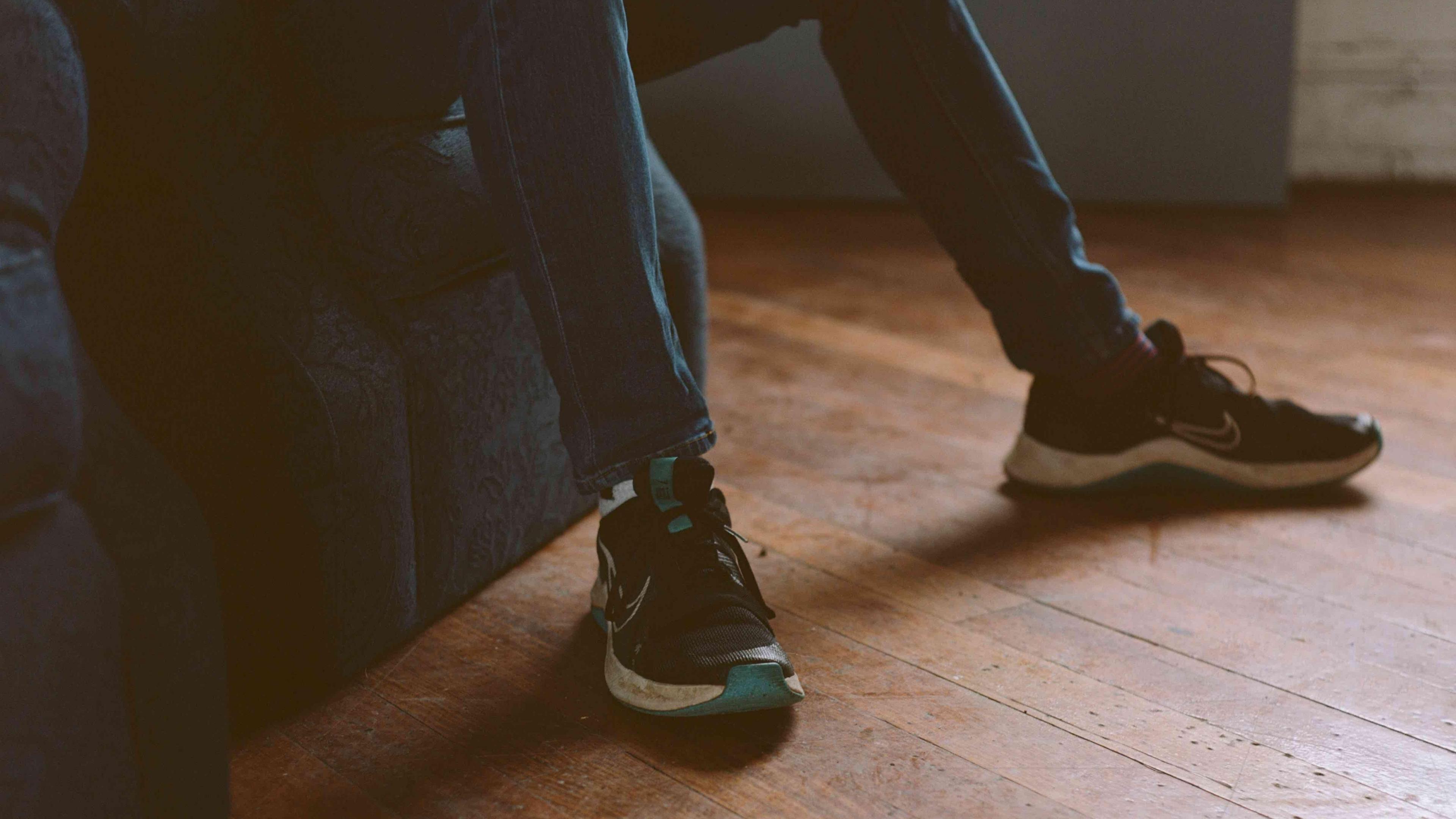 An exhibit image shows the legs of a person sat on a couch. The photo is dark and grainy. The person wears jeans and nike trainers. 