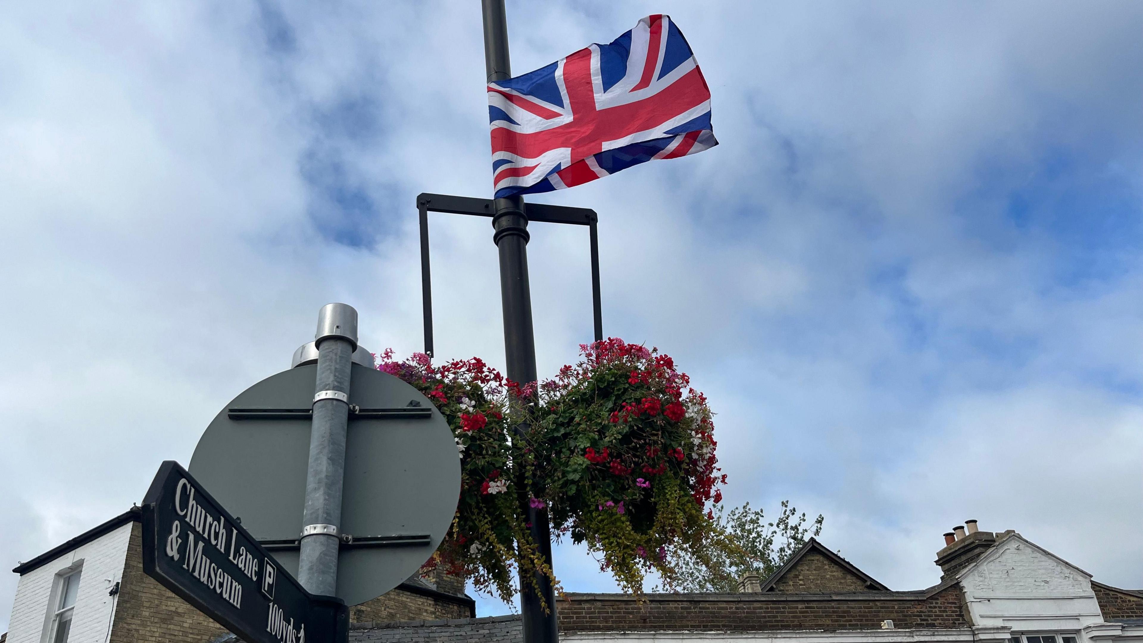 A Union Jack on a lamp-post above some hanging baskets.