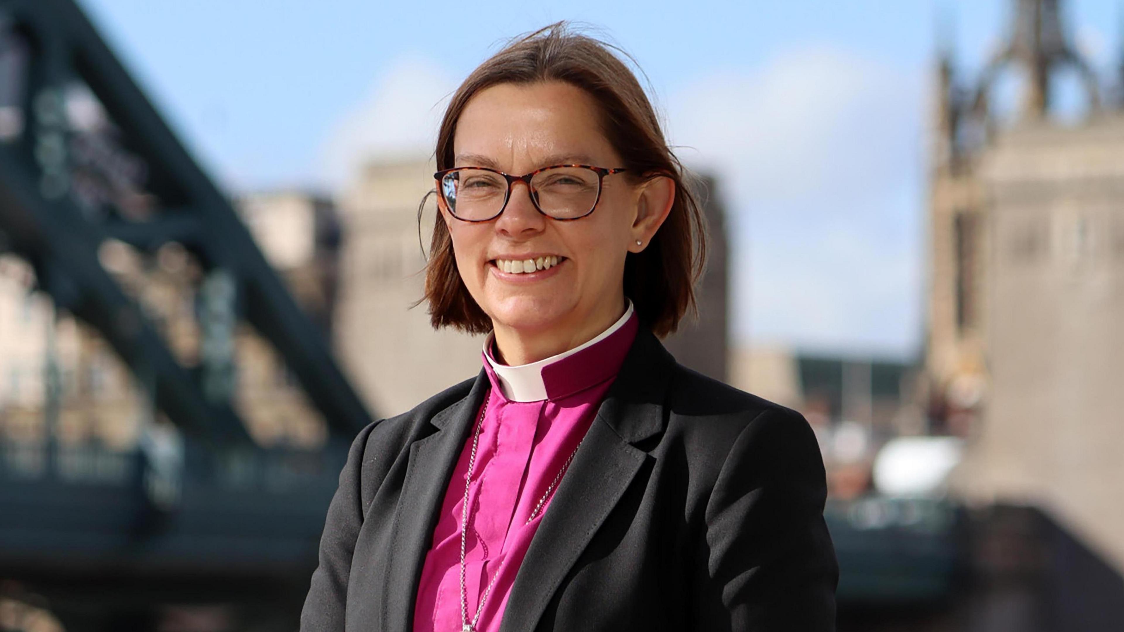 Bishop of Newcastle Helen-Ann Hartley wears a pink robe and brown glasses