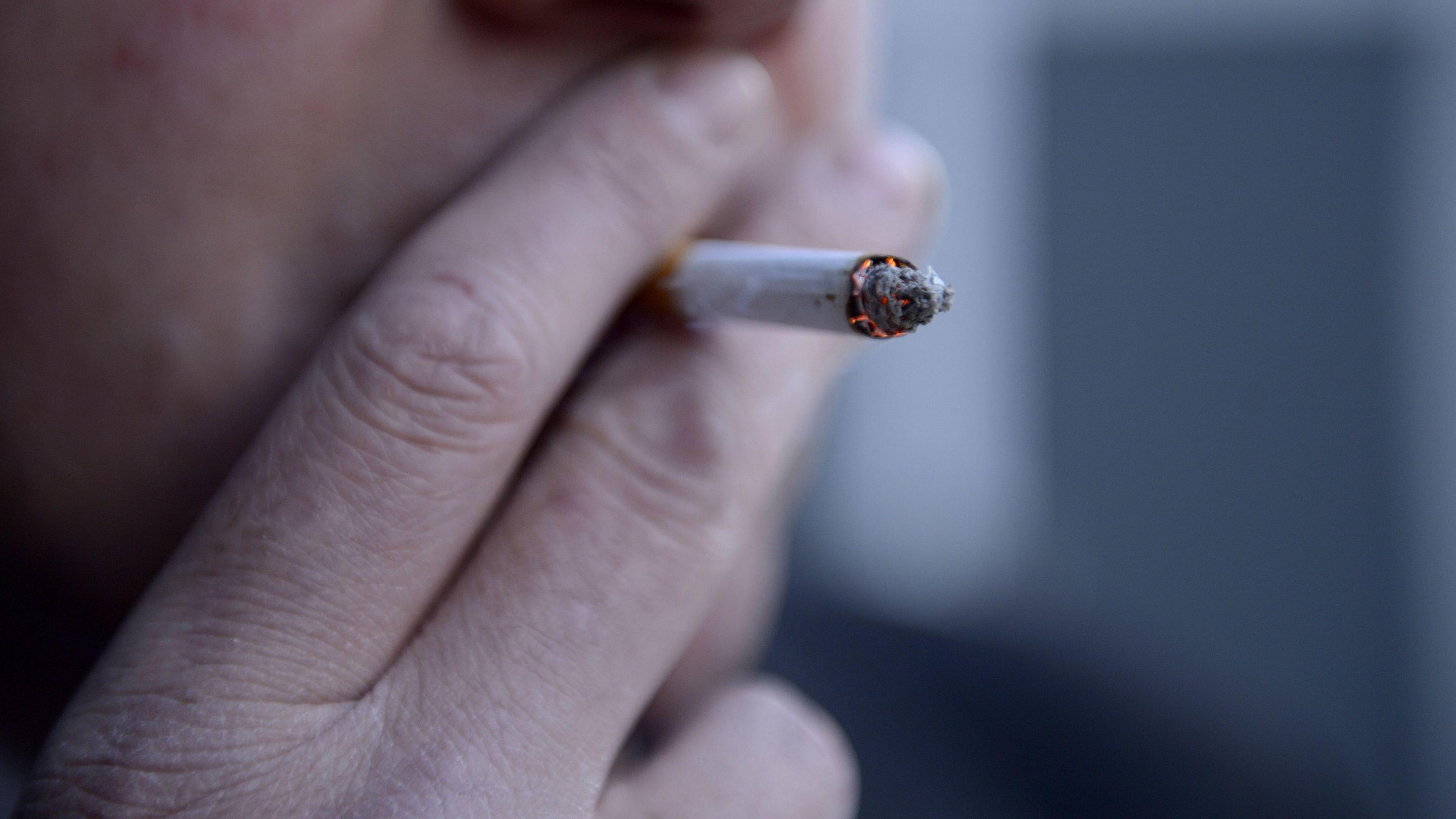 A close-up of a man taking a drag from a cigarette held between his fingers.