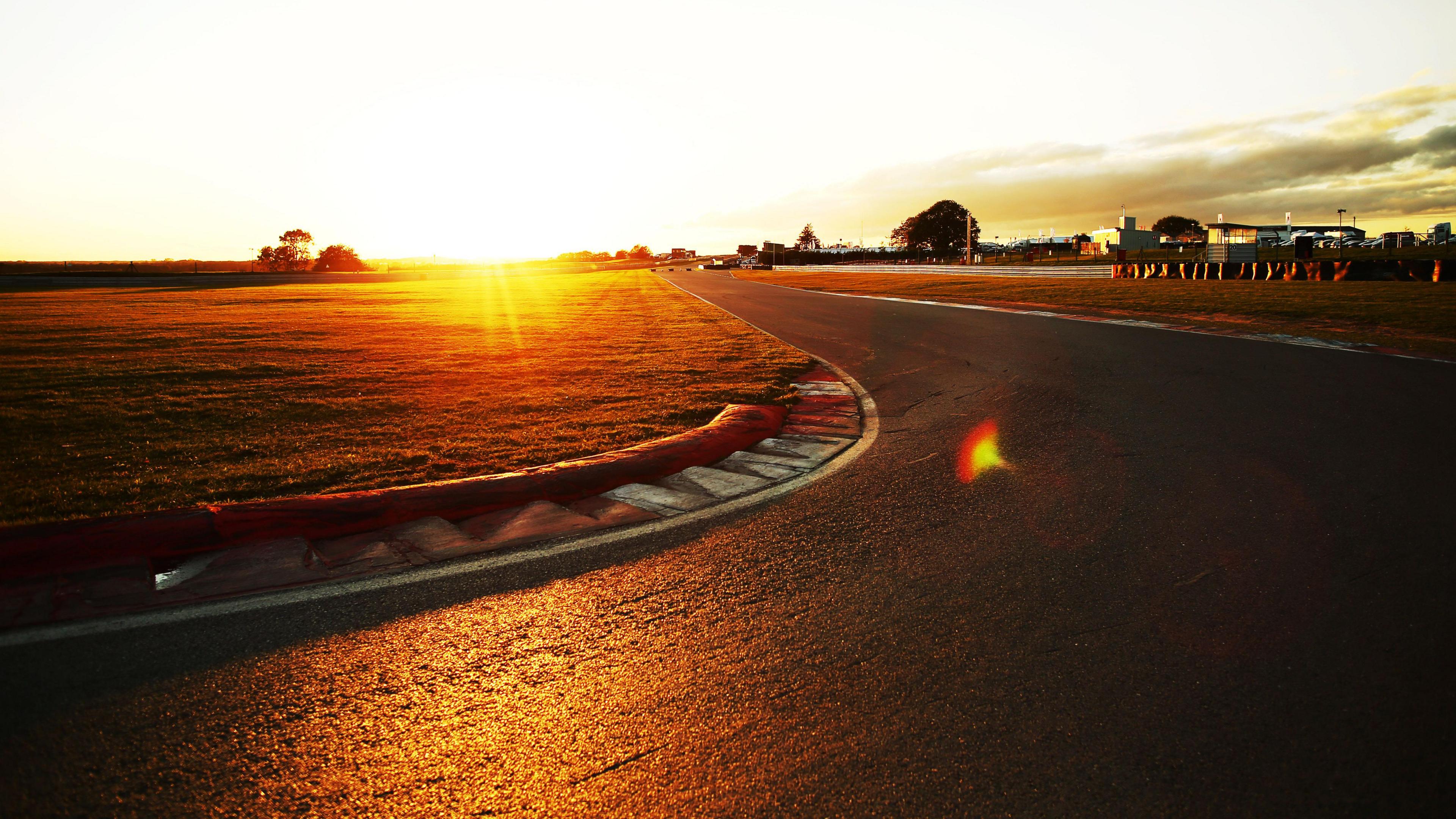 Snetterton racetrack, with the sun in the distance, you can see a track, grass area and a number of buildings in the distance, to the right. 