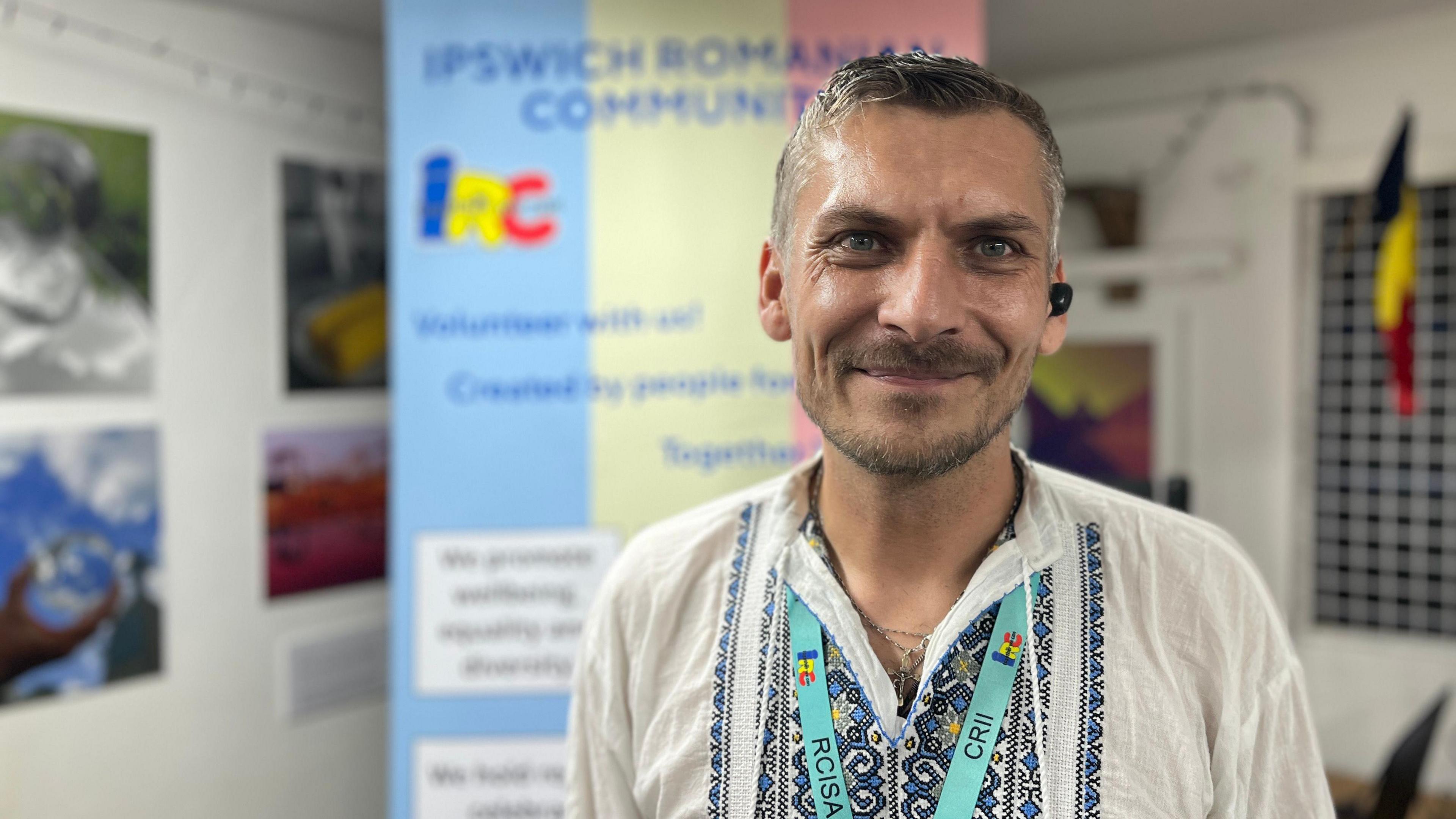 Romeo Mustata stands in front of a pop-up banner for the IRC group. He has short greying hair and a beard. He appears to be at least in his late 30s or early 40s.