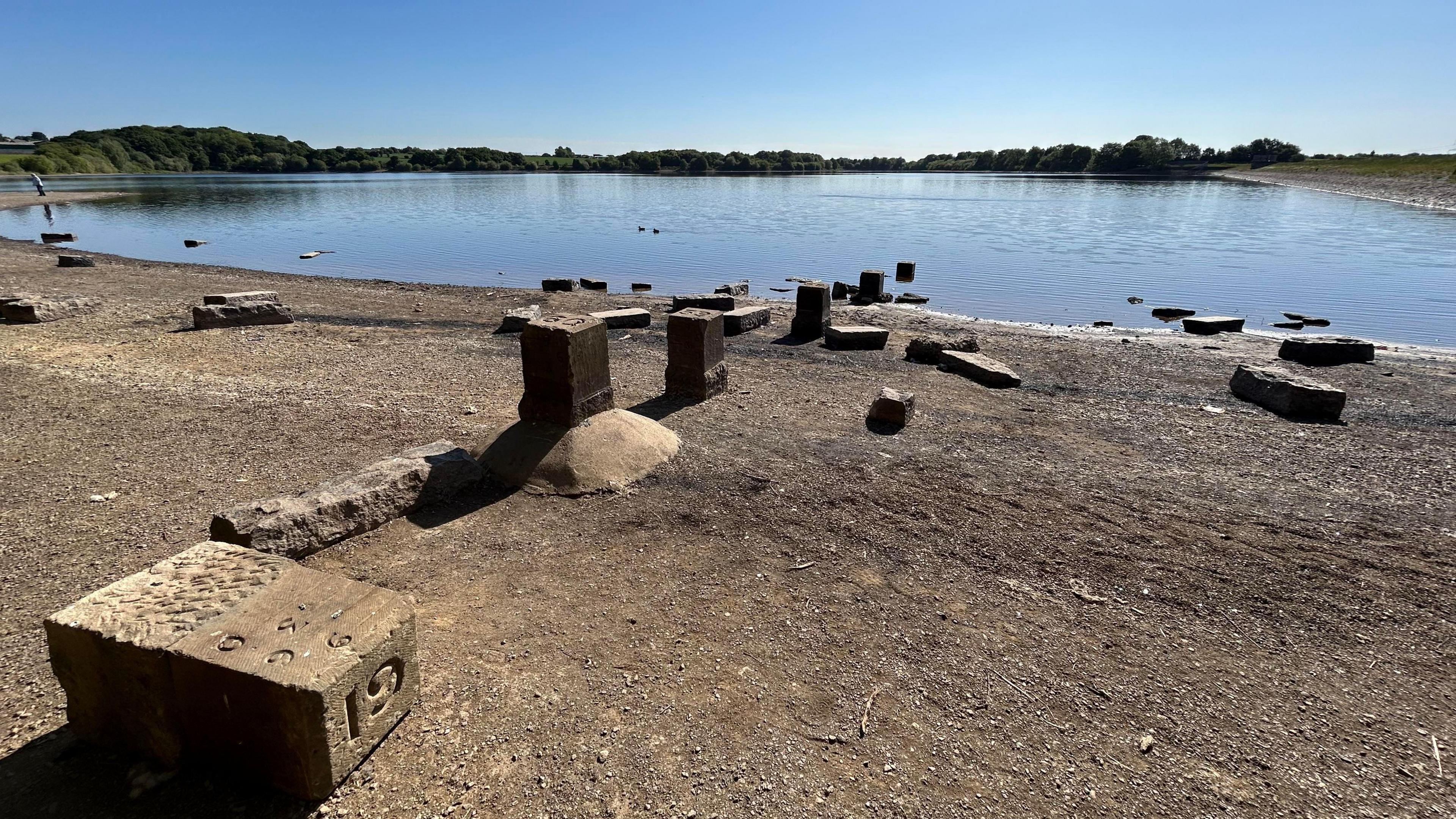 A low reservoir with a sandy reservoir floor exposed and several stone blocks on the shore. 