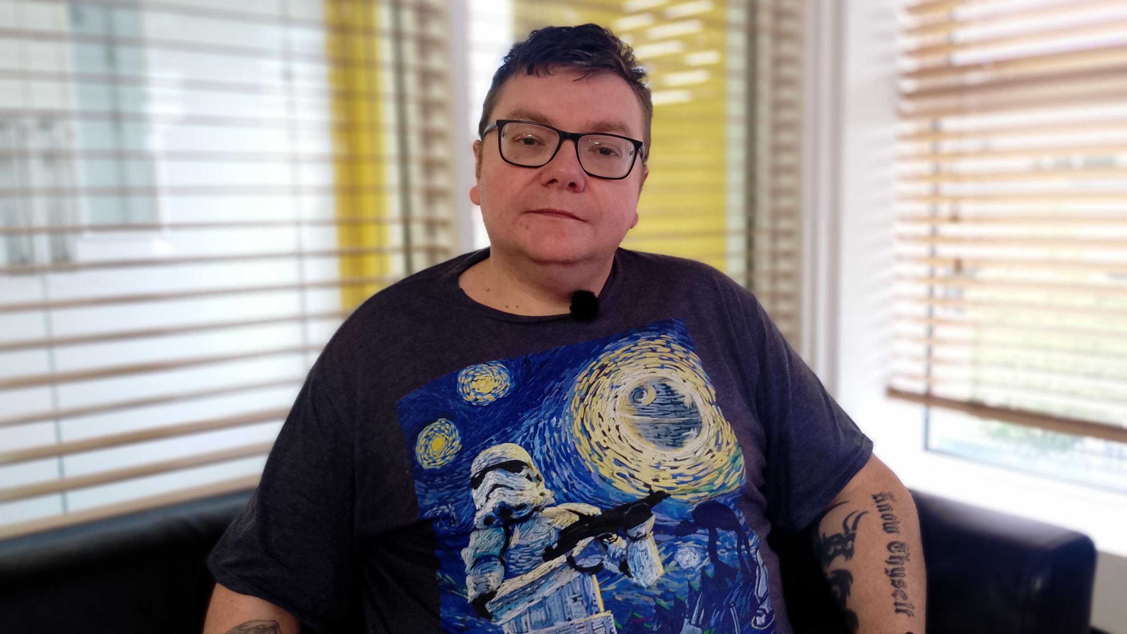 Steven Herron wears a navy T-shirt with a Van Gogh Starry Night inspired pattern. He has black glasses and short brown hair. 
