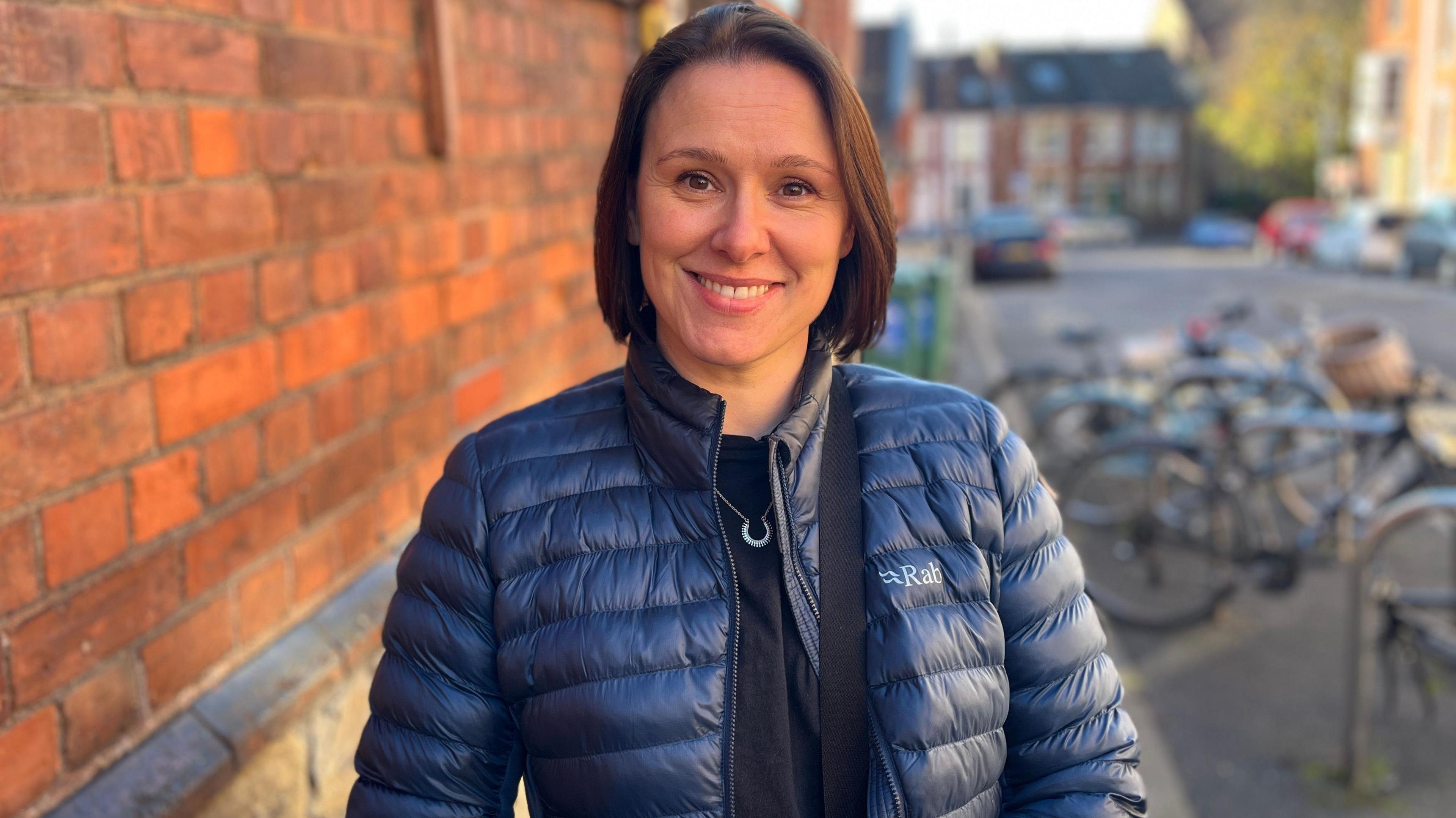 Jacqui Manning. She has short dark hair and is wearing a navy blue puffer coat. She is looking at the camera and smiling.