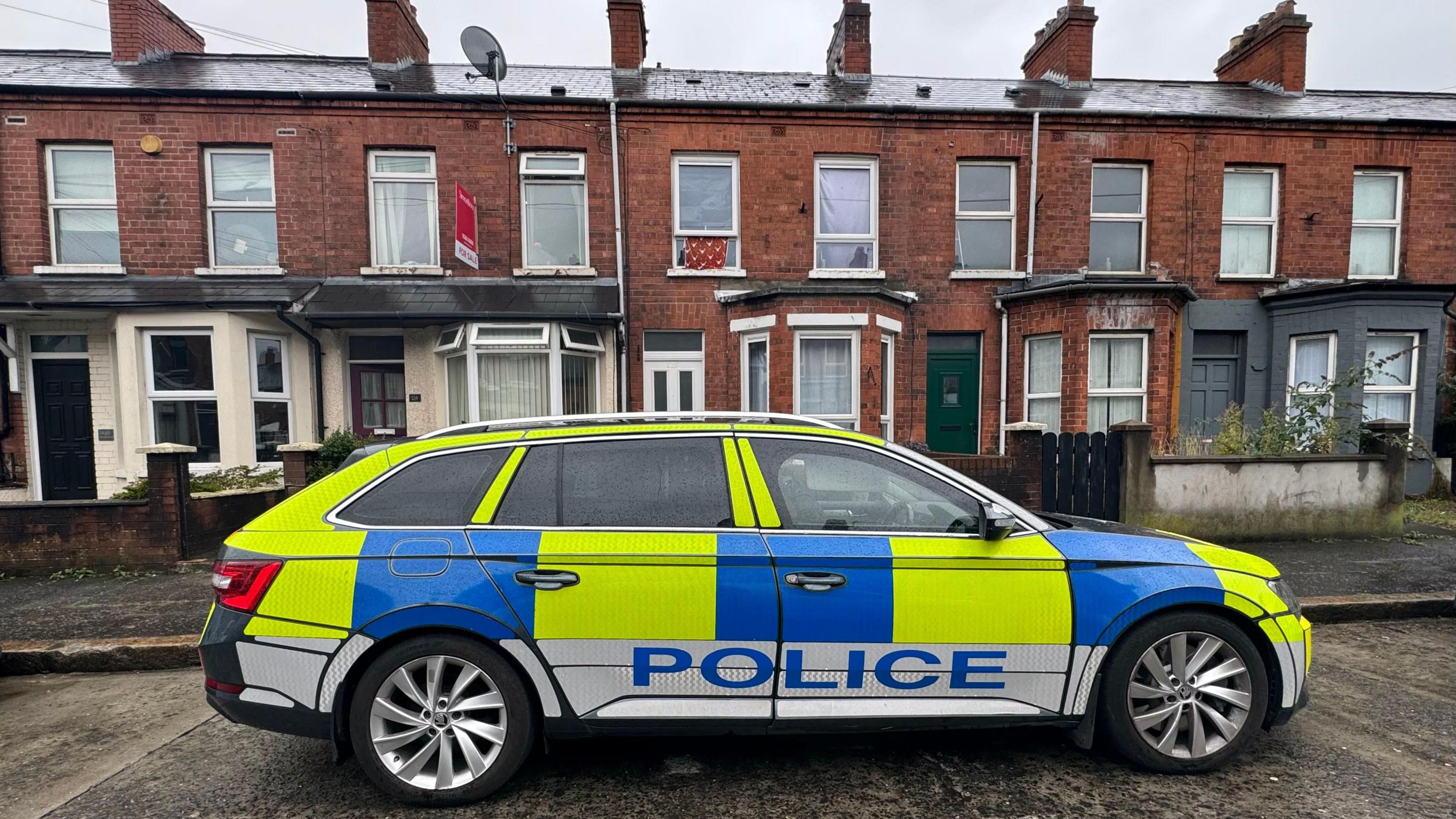 A police car parked outside a row of red brick terrace houses in Belfast