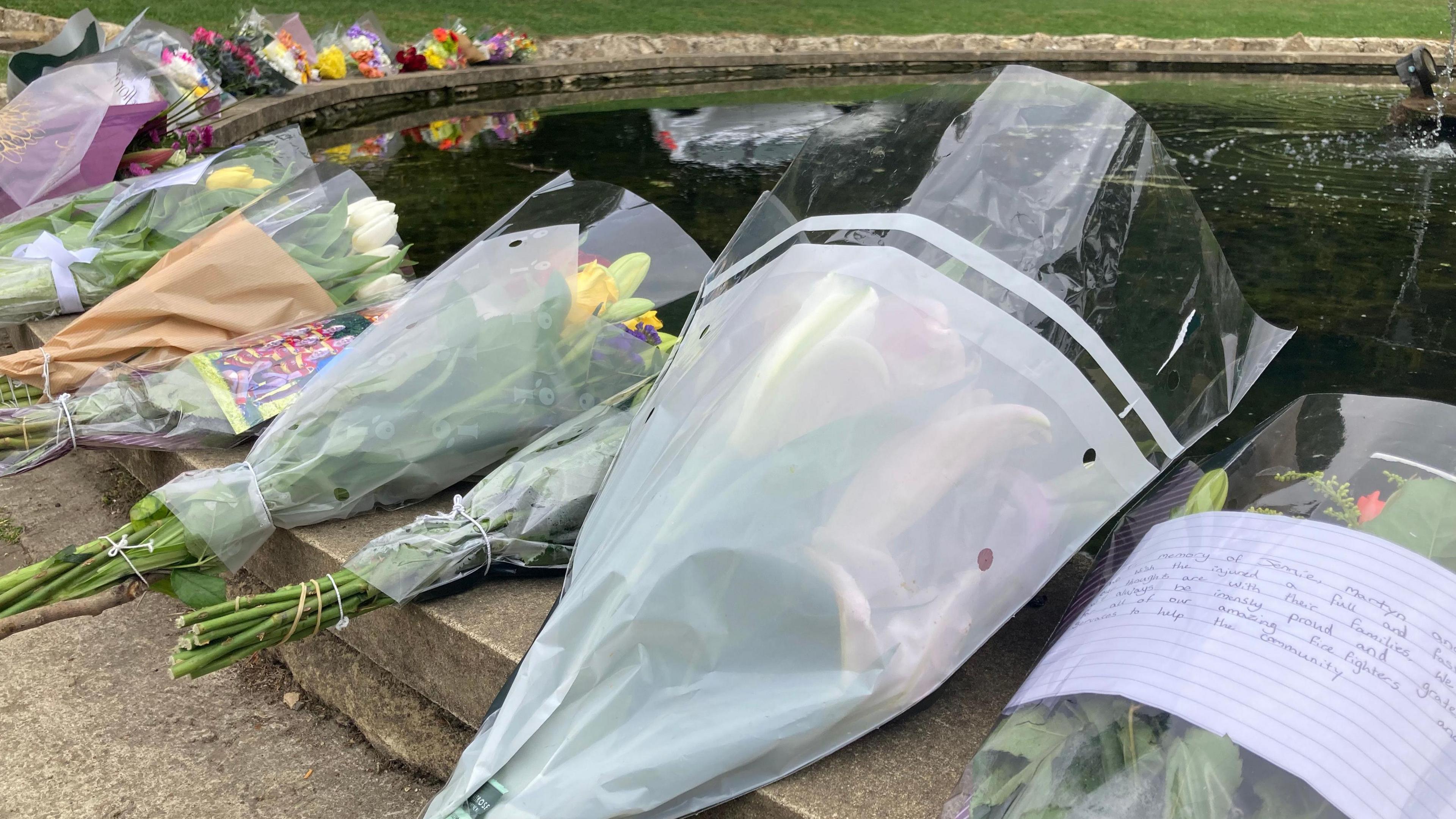 Wrapped bunches of flowers laid on the stone edge of a round pond with a fountain in the centre.