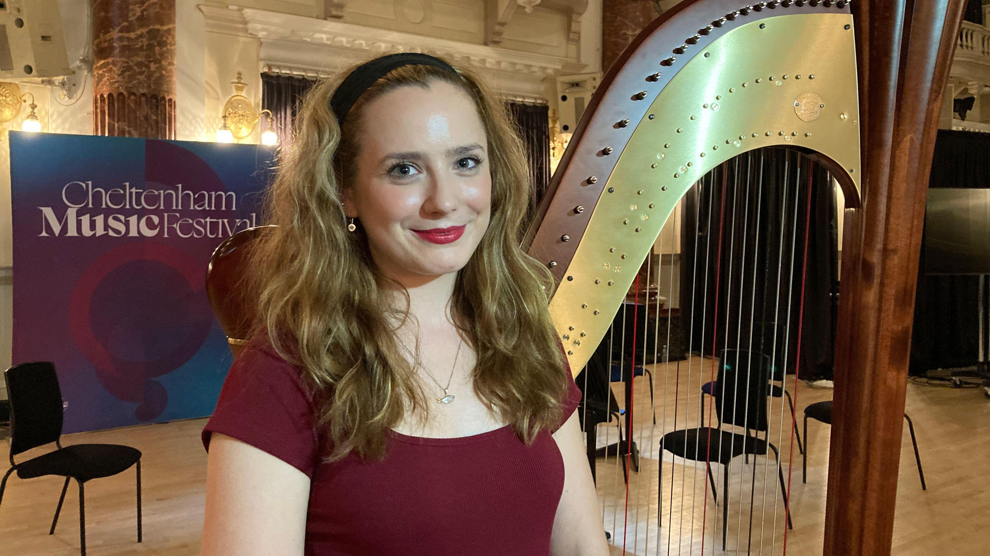 Emily Hopper, harpist smiling at the camera wearing red dress.