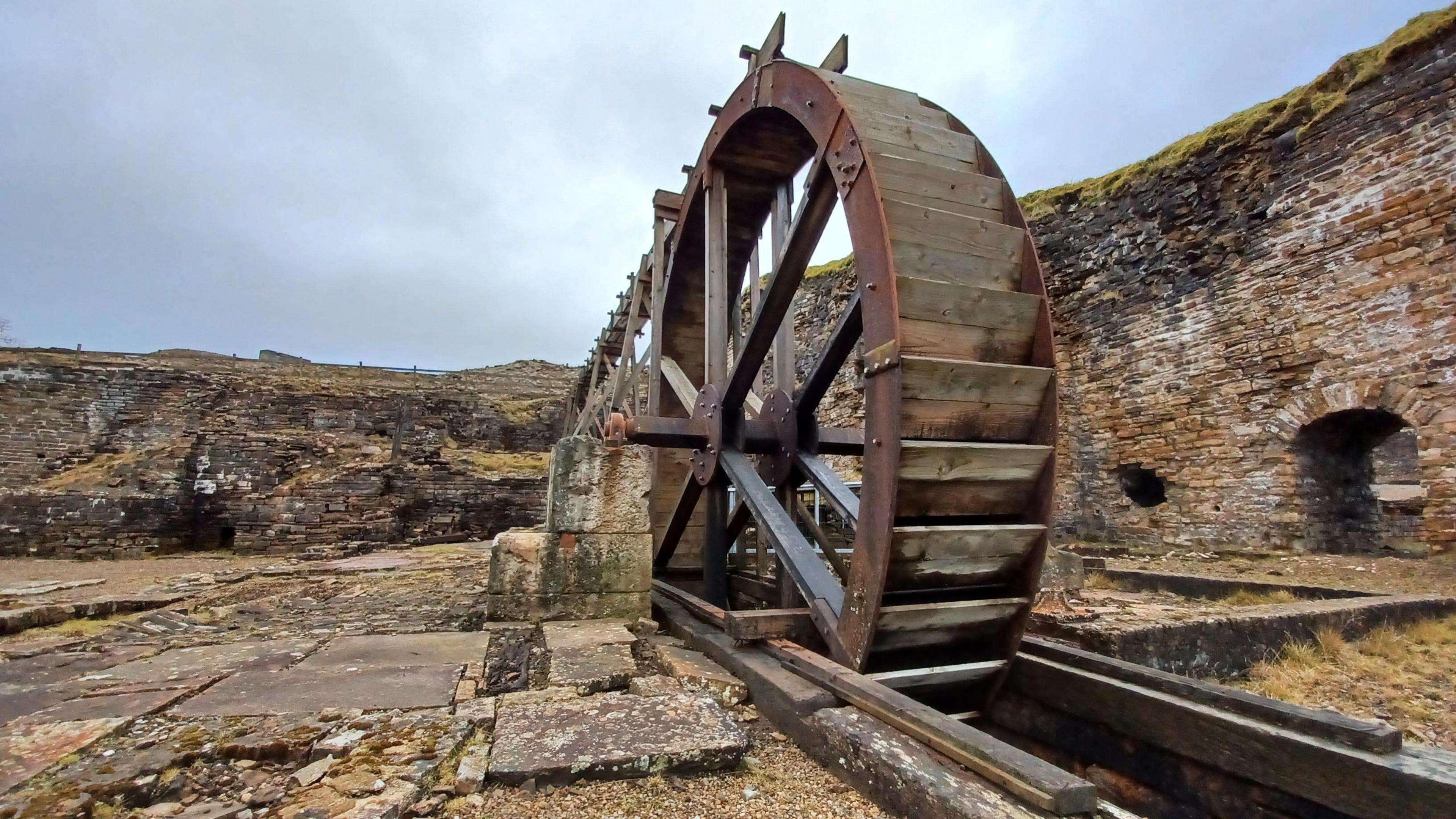 Free standing water wheel with raised structure to feed it, in what looks like a quarrye 