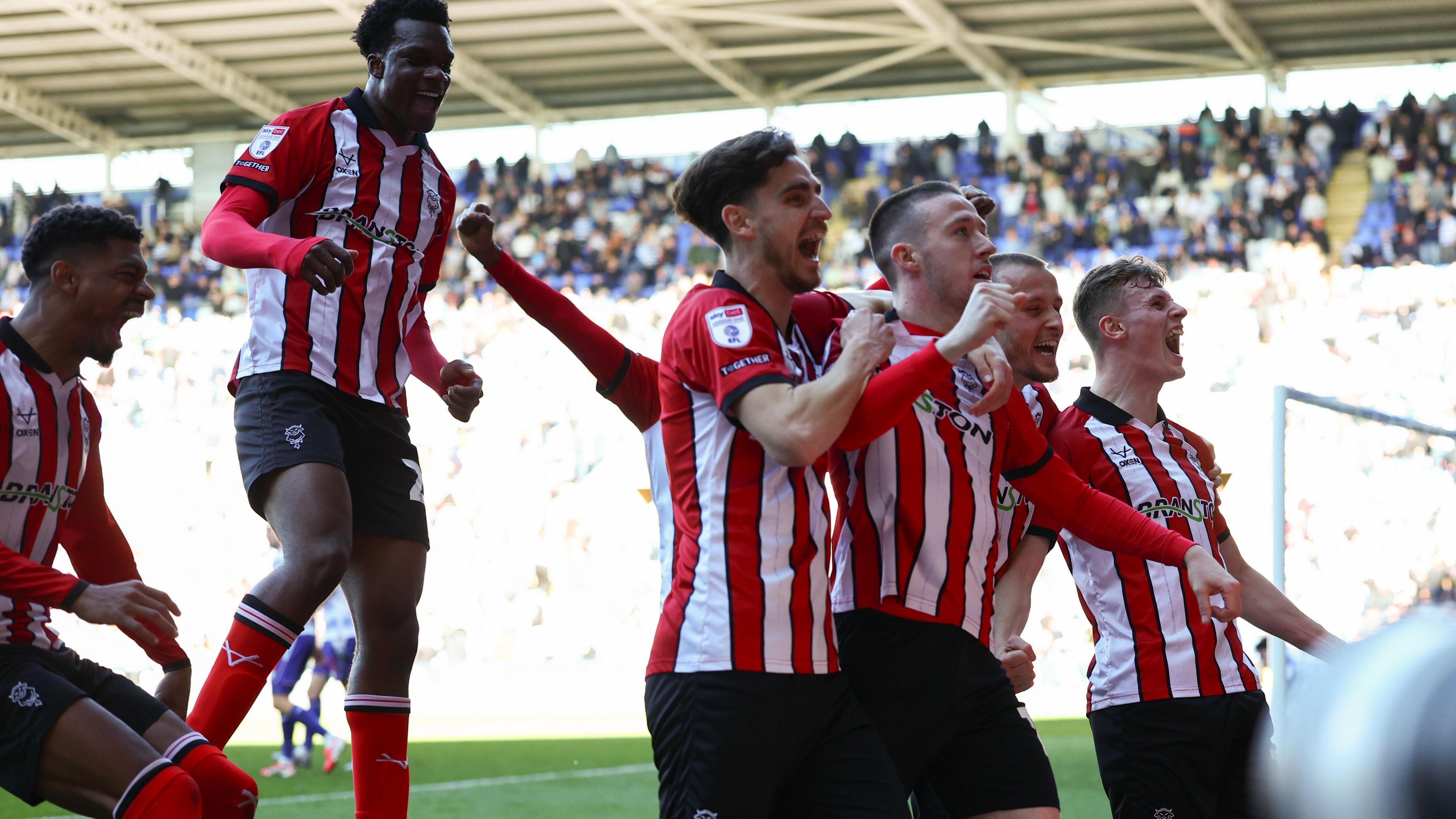 Jack Moylan is embraced by Lincoln City team-mates after scoring the goal that sealed victory against Reading and promotion to the Championship