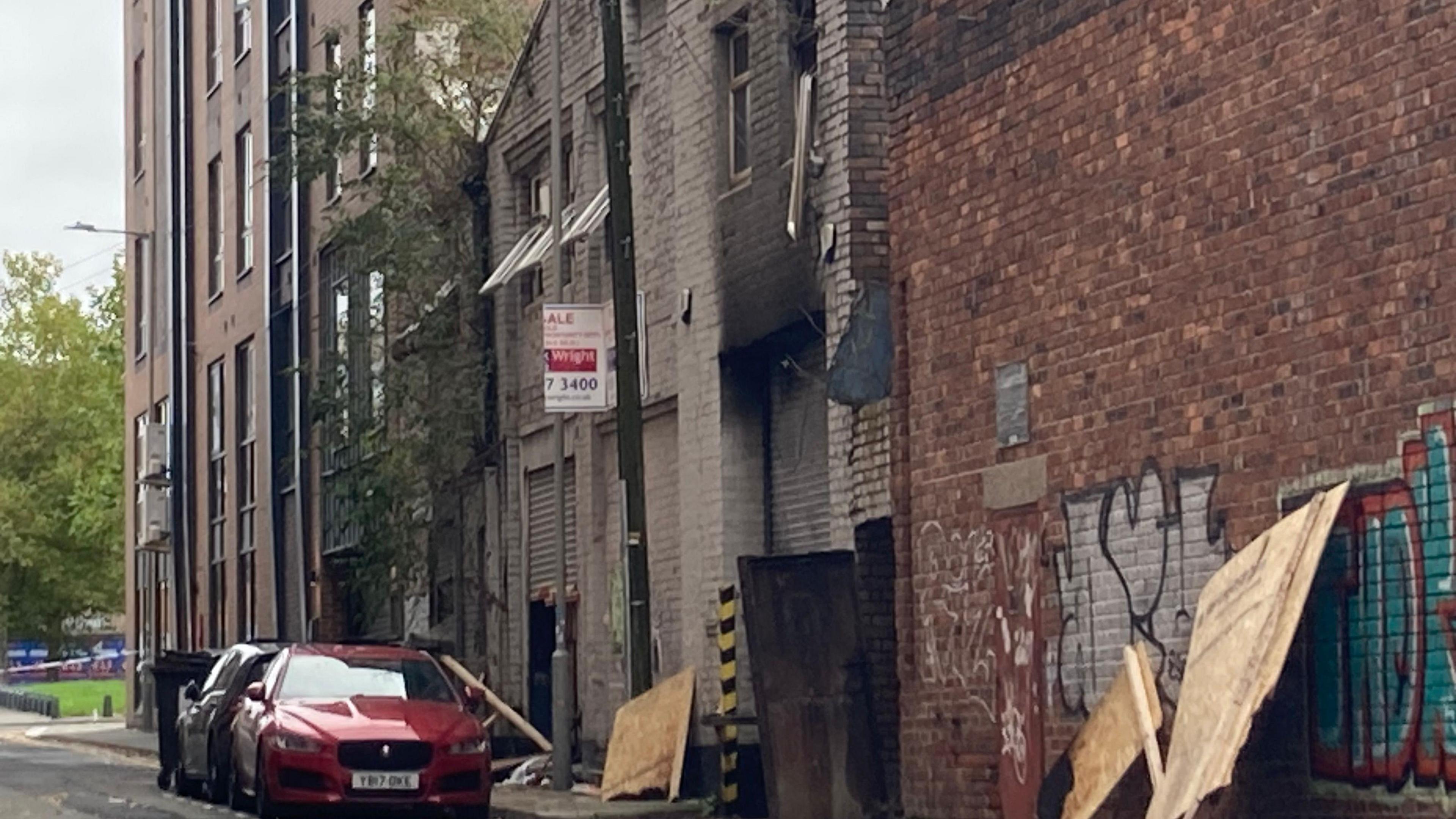 The building has fire damage, with some charred areas. Debris can be seen outside the building, including some wooden panelling.