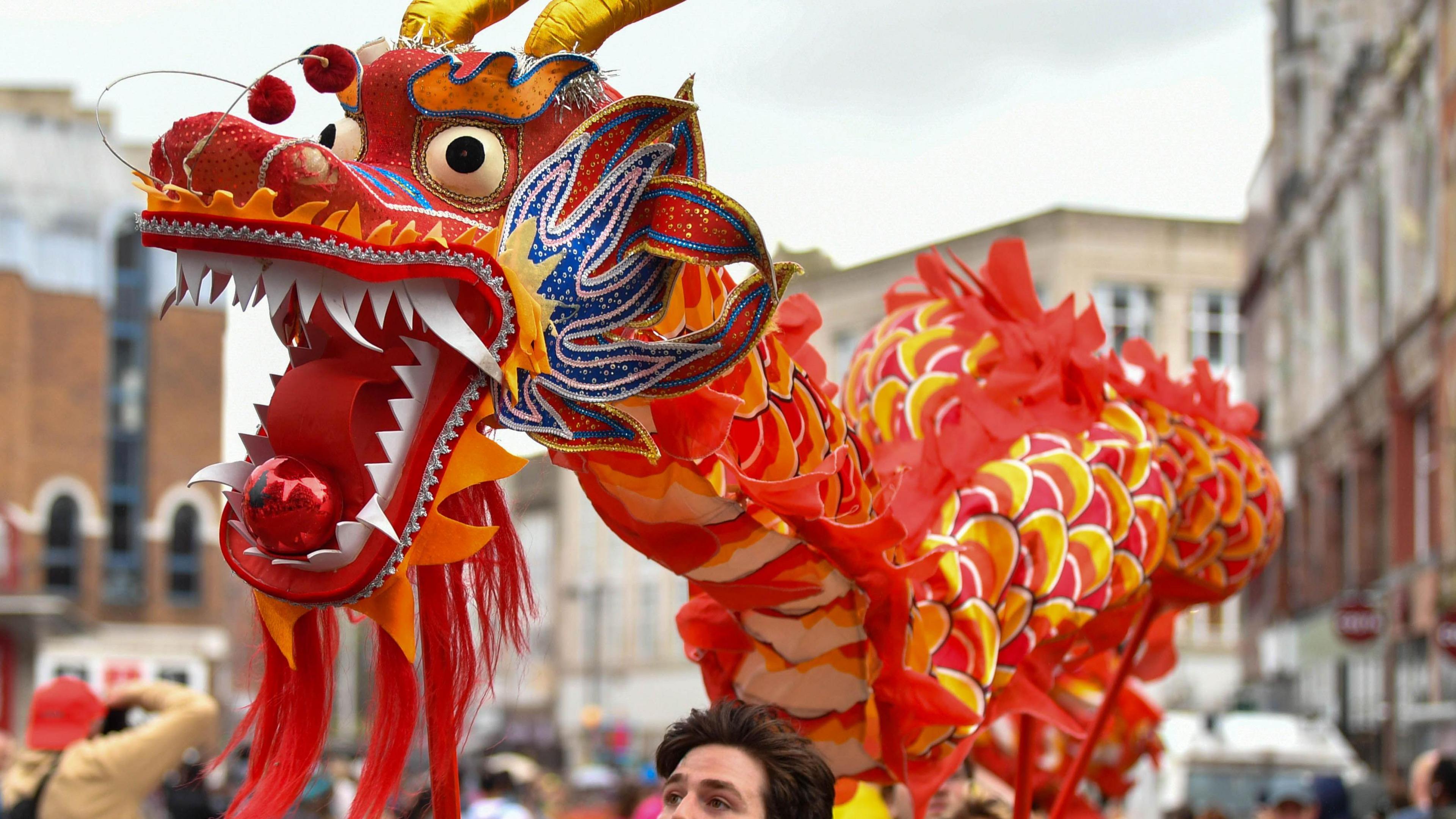 Chinese dragon float, which is mostly red and yellow, being held aloft