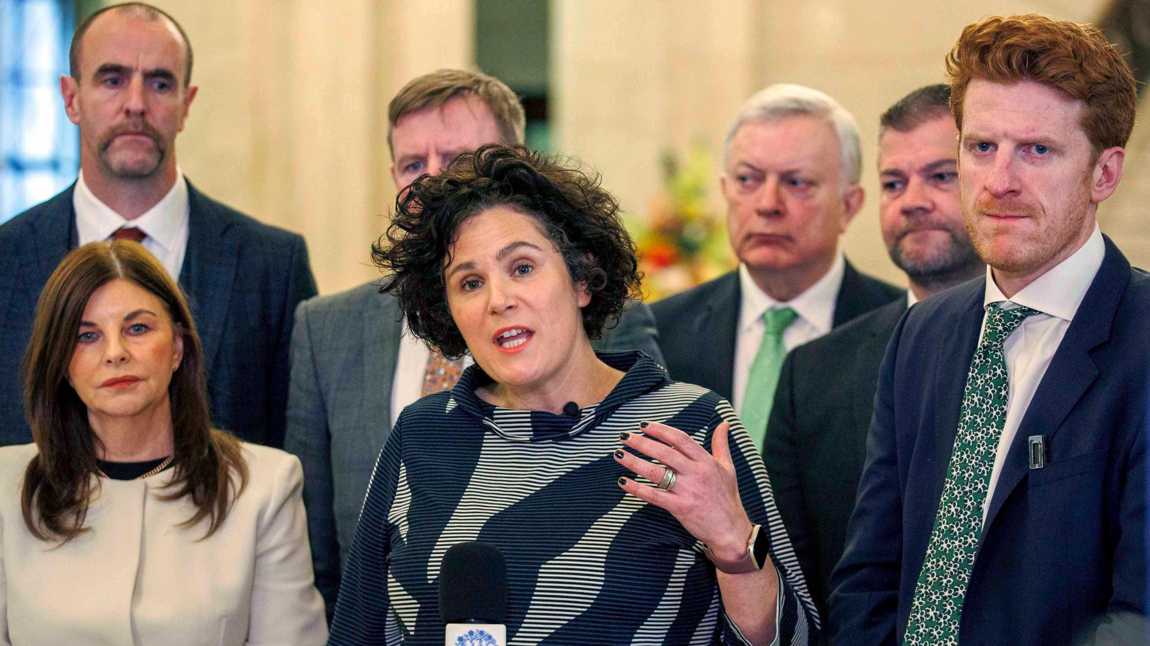 Claire Hanna with her SDLP with the party MLA's speaks to the media during a press conference in the Great Hall, Parliament Buildings. Wearing a black and white stripped cardigan looking at the camera.