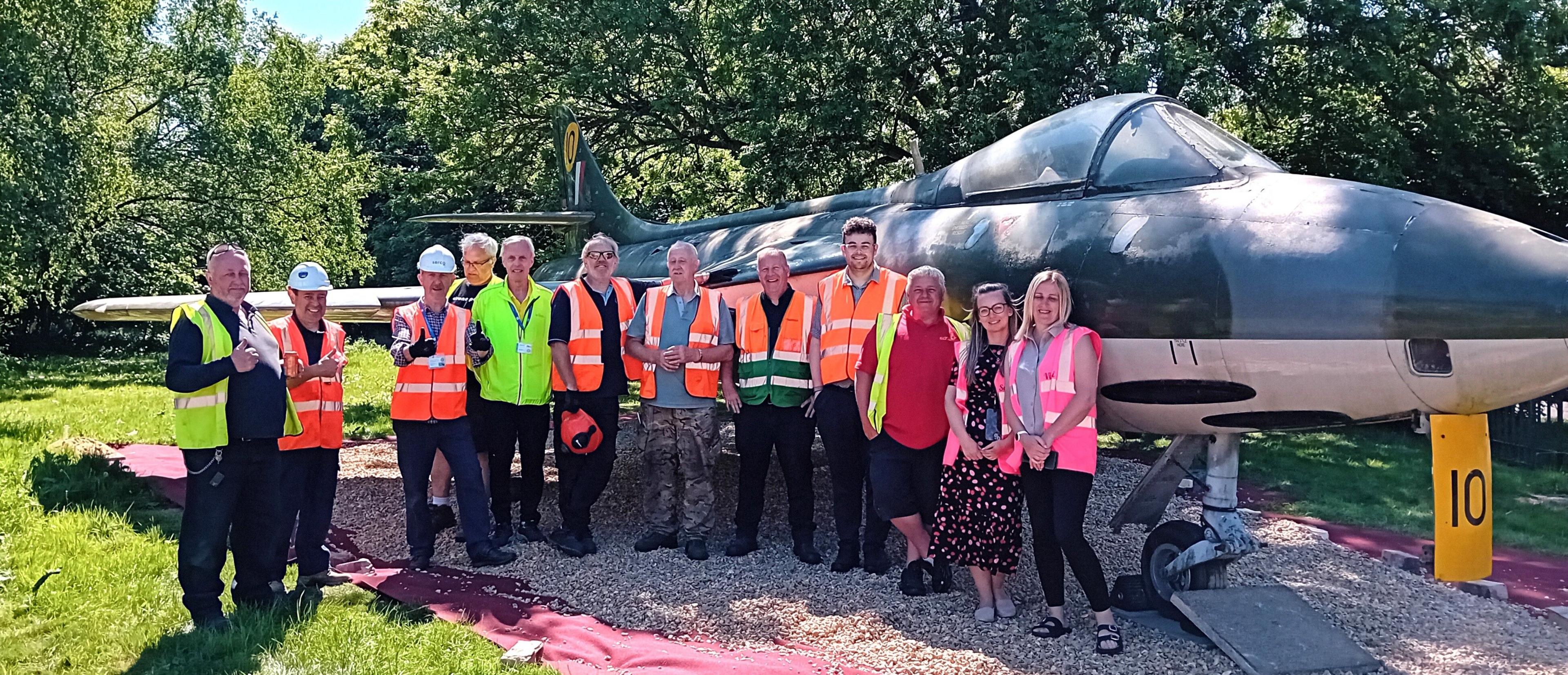 A line of people in hi-vis vests some wearing hard hats celebrate the jet being in its new home.