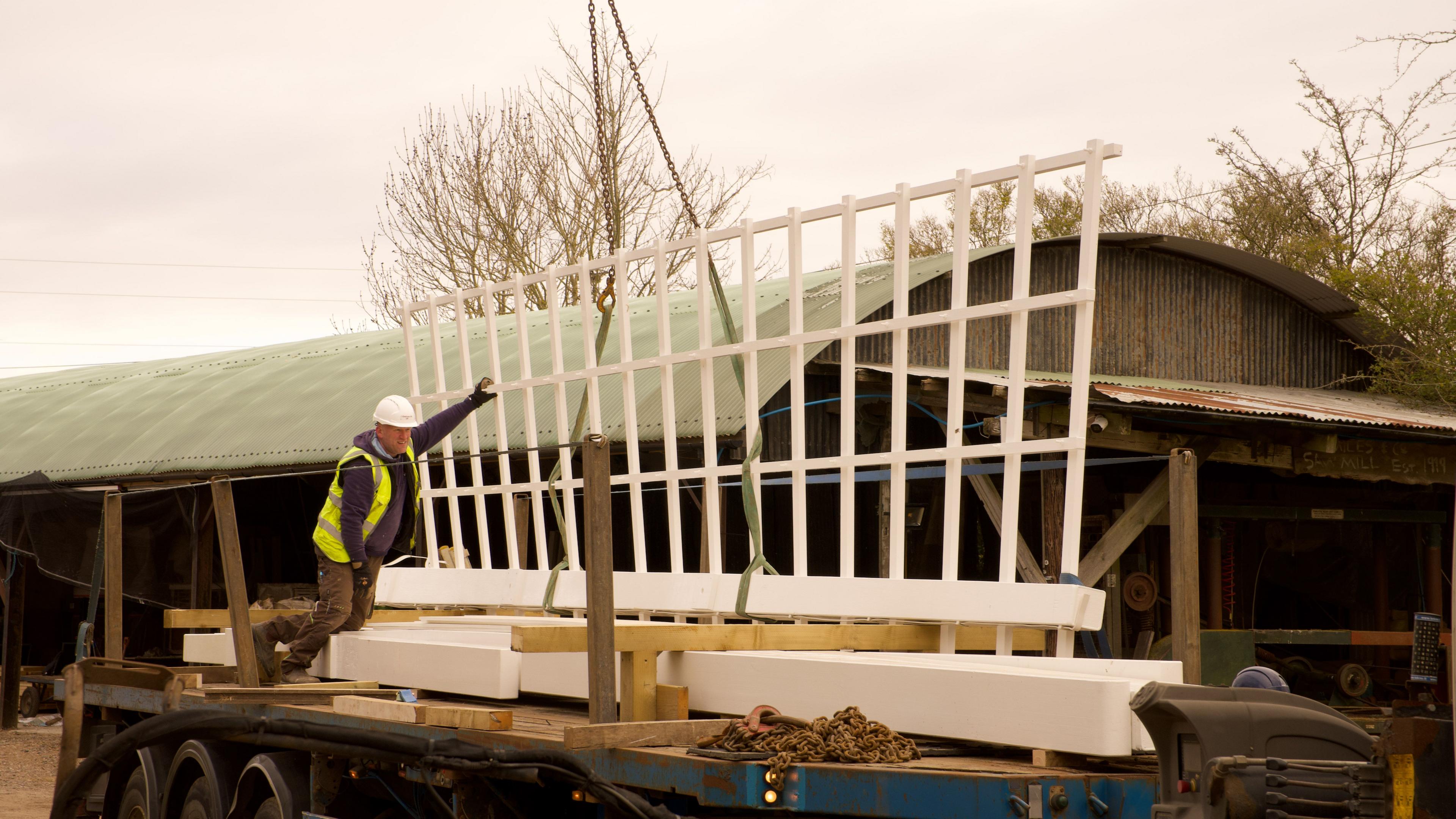 A man wearing a high vis jacket and white hard hat guides a sail into place on a lorry.