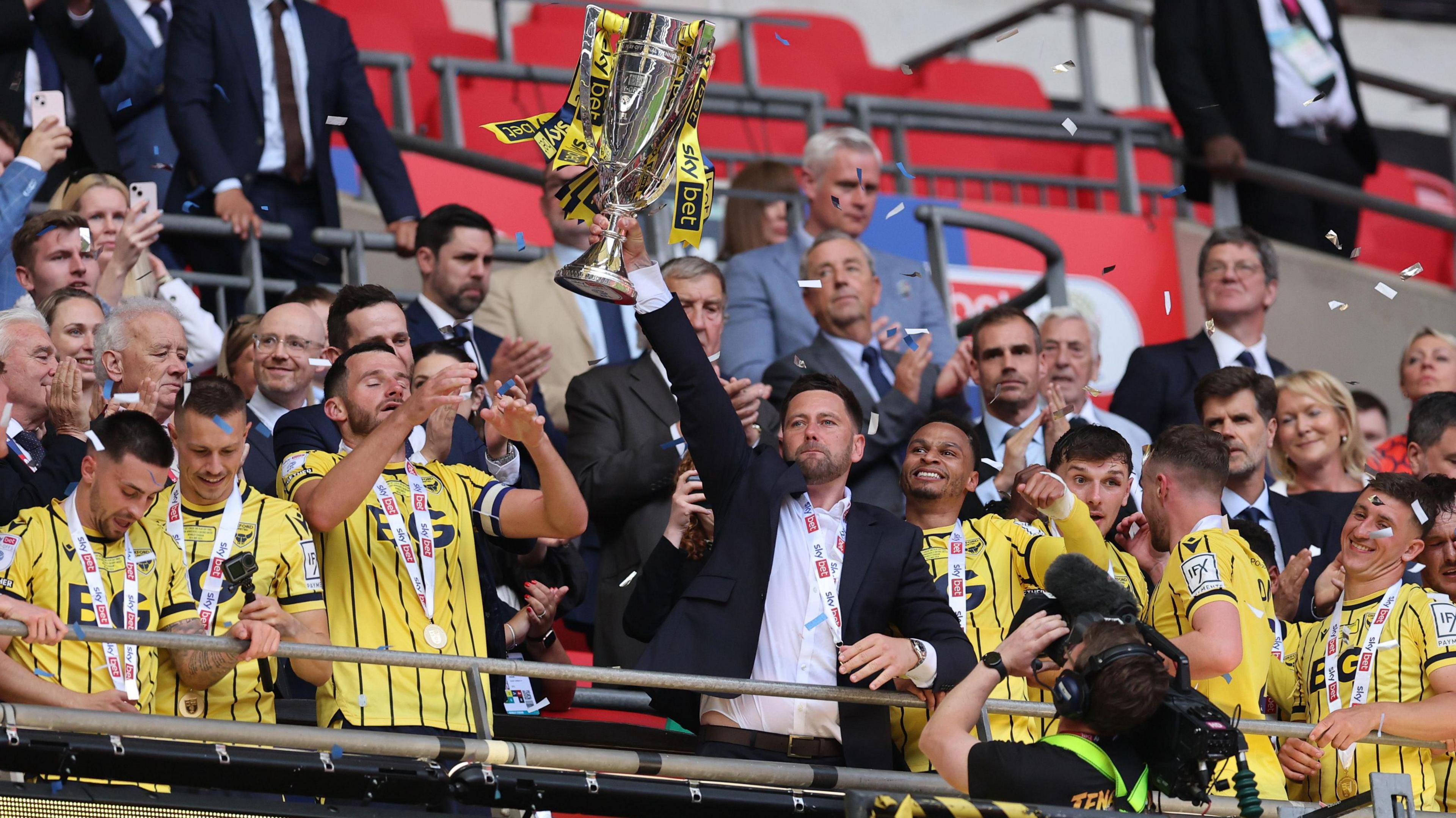 Oxford United manager Des Buckingham holds the 2023-24 League One play-off trophy aloft at Wembley