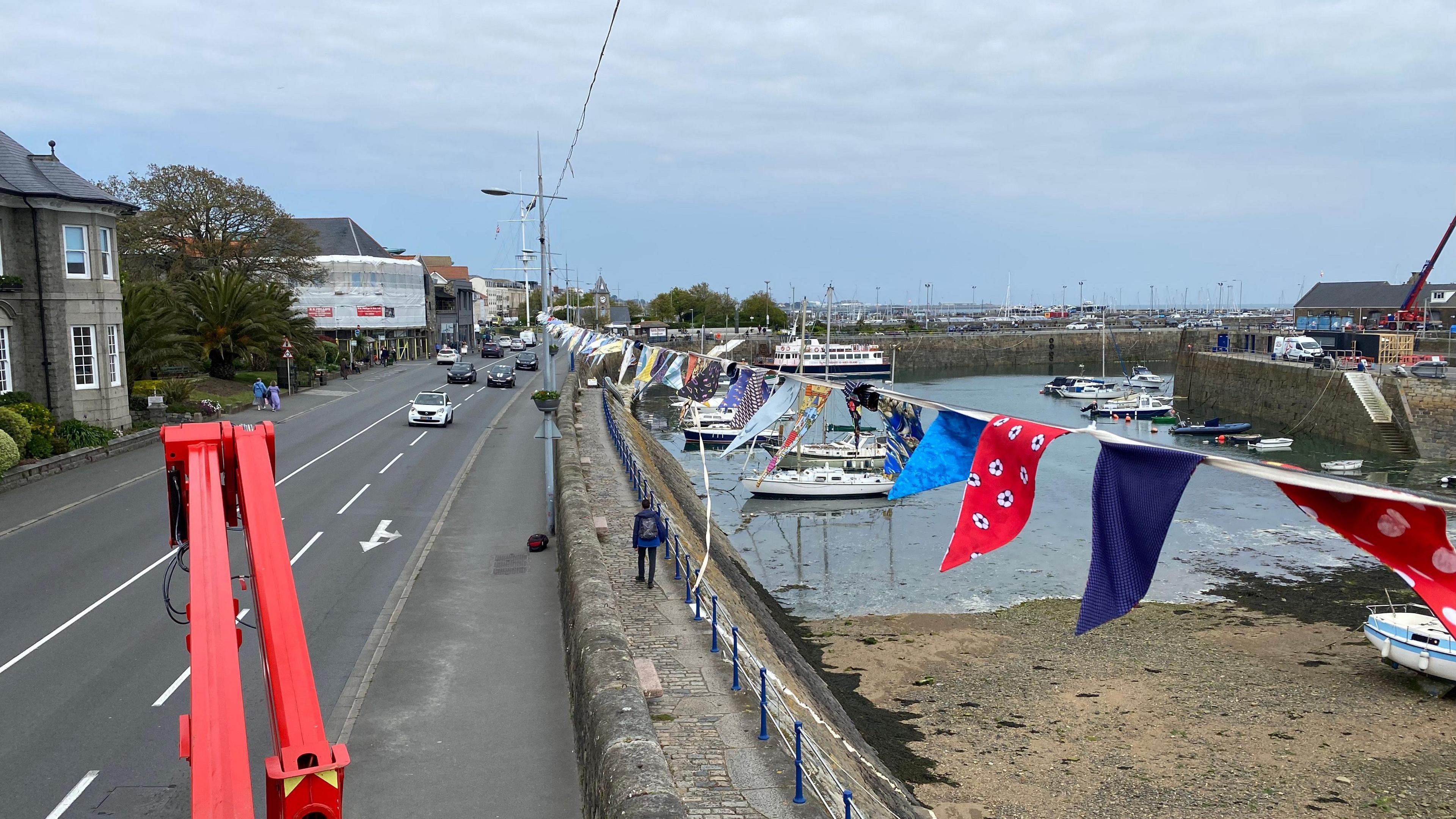 Bunting hung over along a main road with the road to the left of the bunting and the sea to the right. 