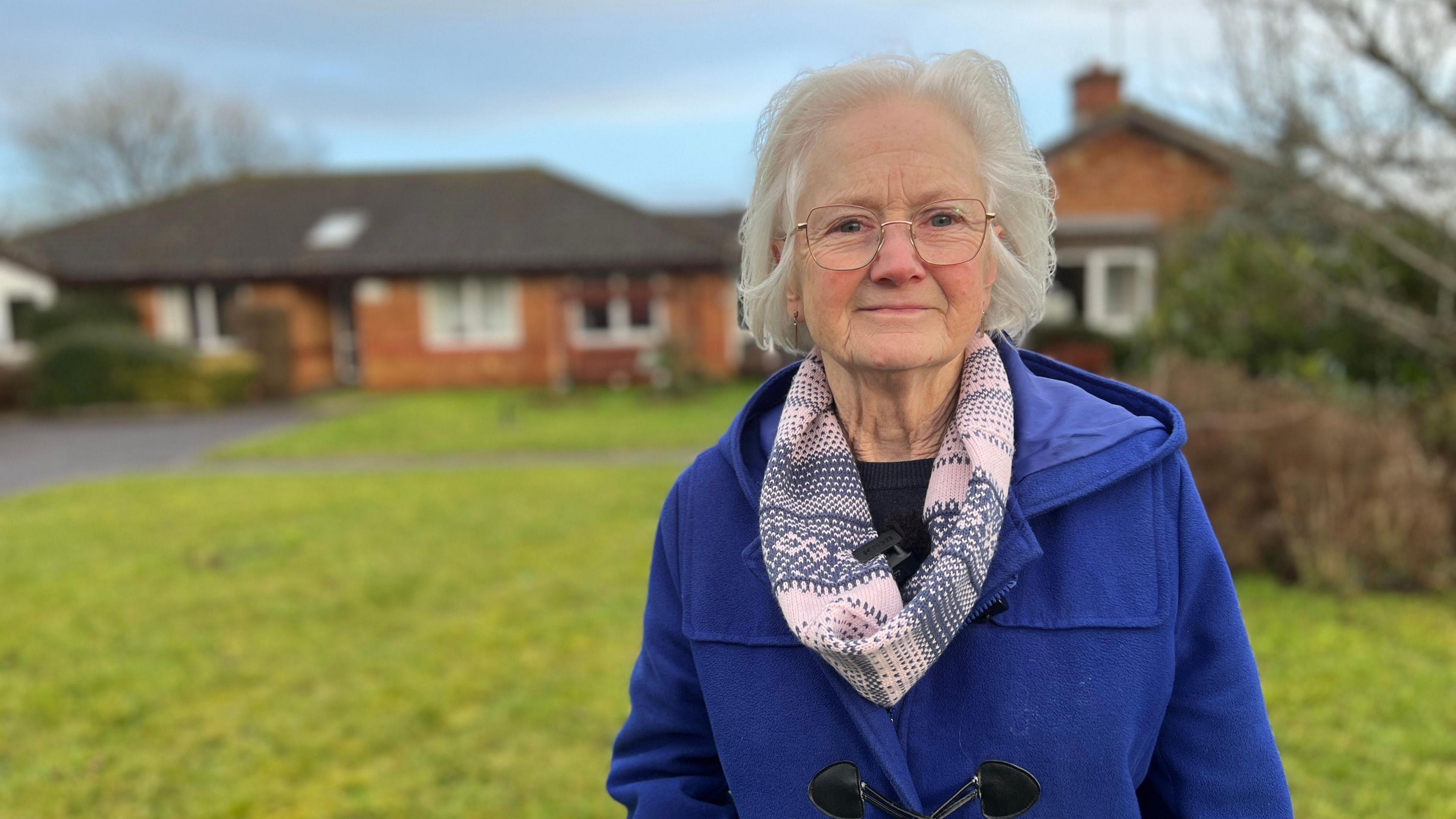 Trish Gange, an older woman in a blue duffel coat, standing outside Furlong Close, which is blurred in the background