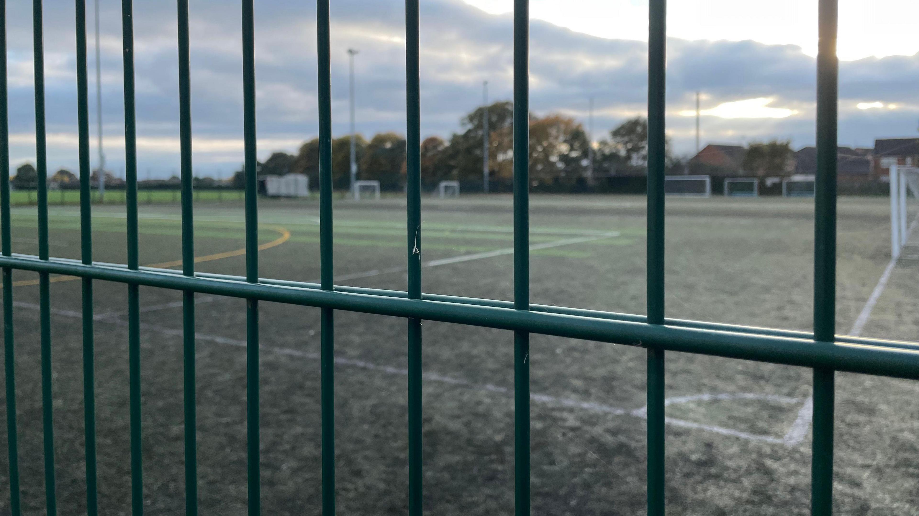 An artificial grass football pitch behind bars of green painted metal fence