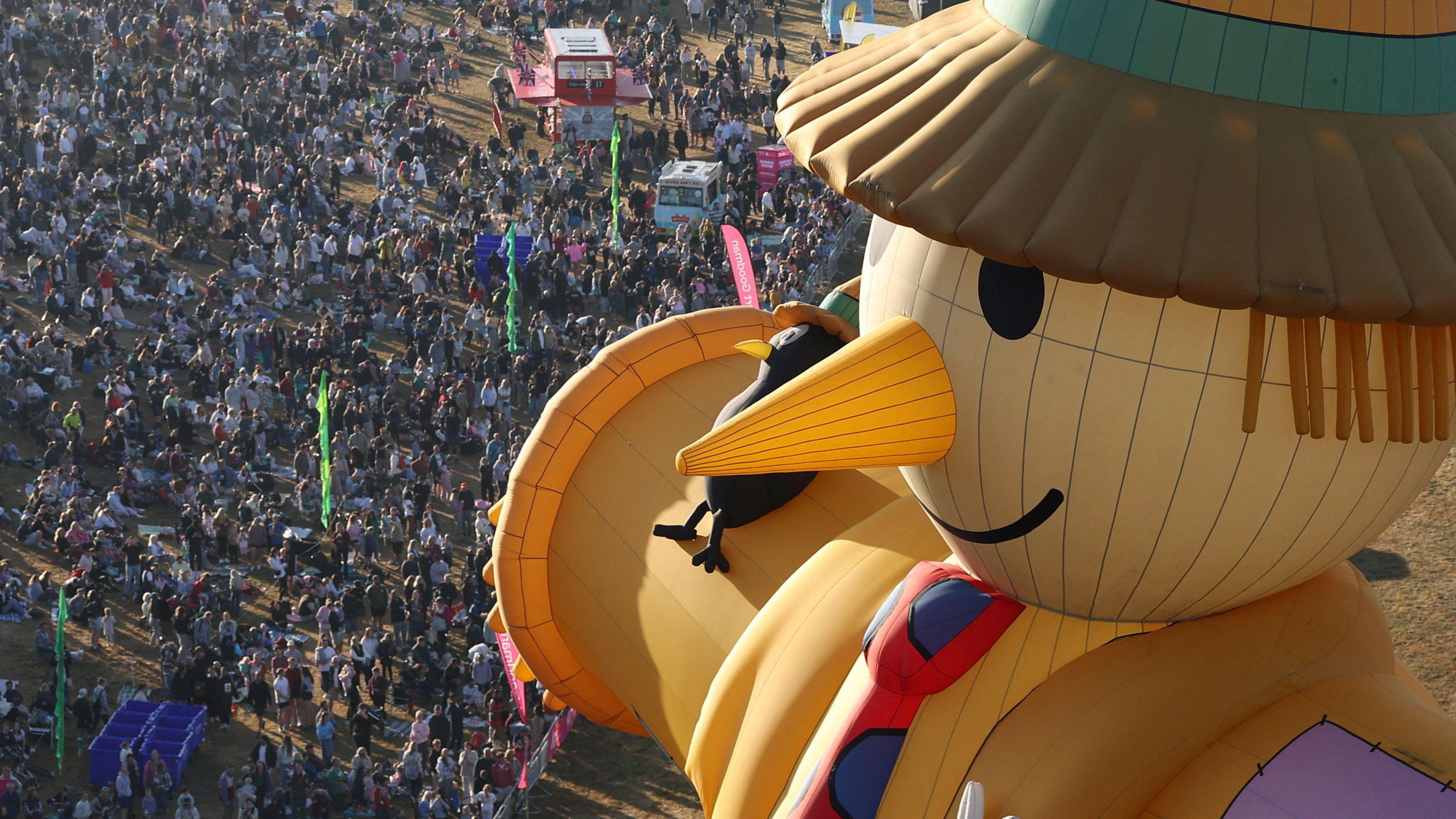 A scarecrow hot air balloon flying over a crowd of people.