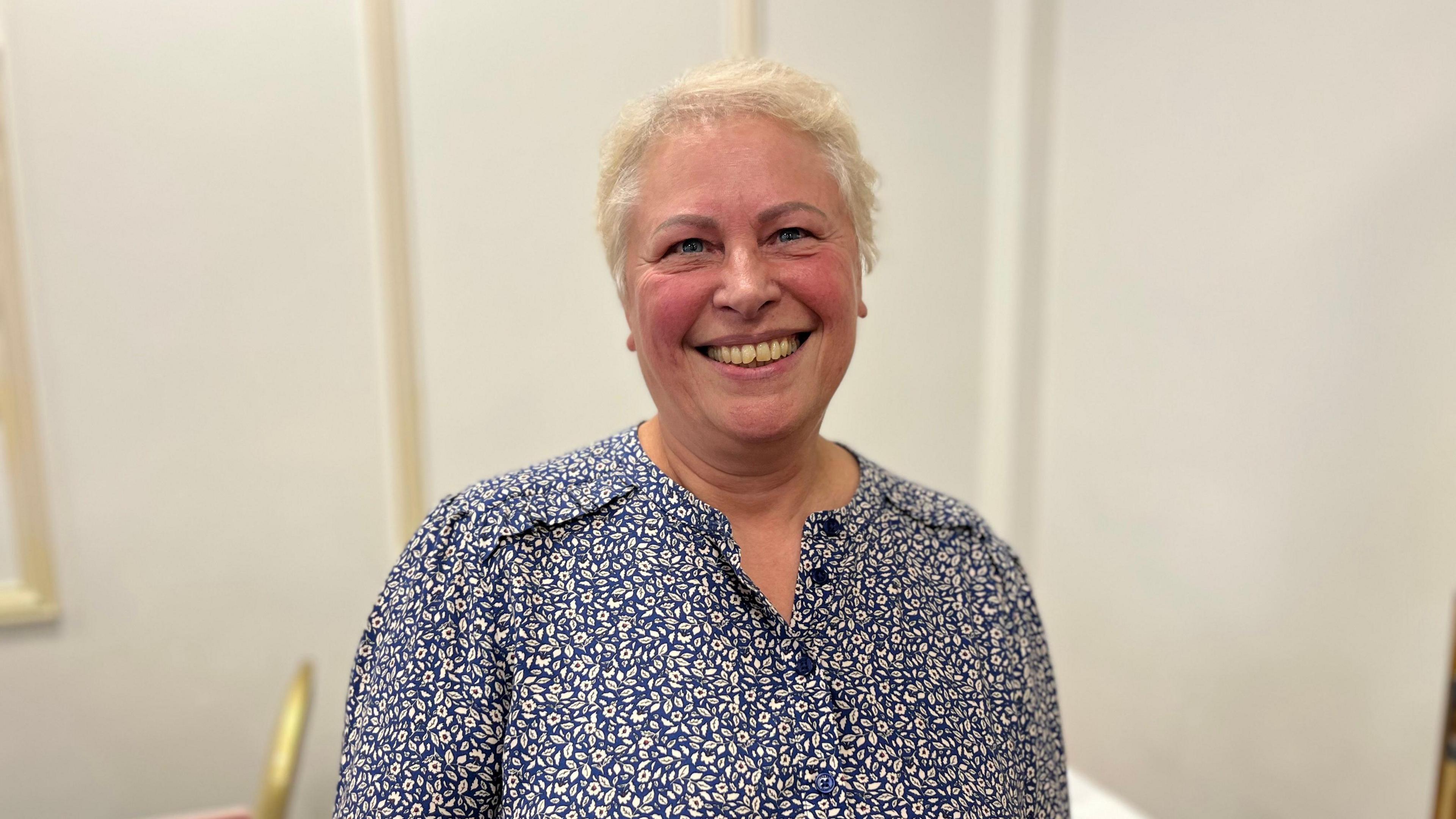 A woman in a patterned top and fair hair.