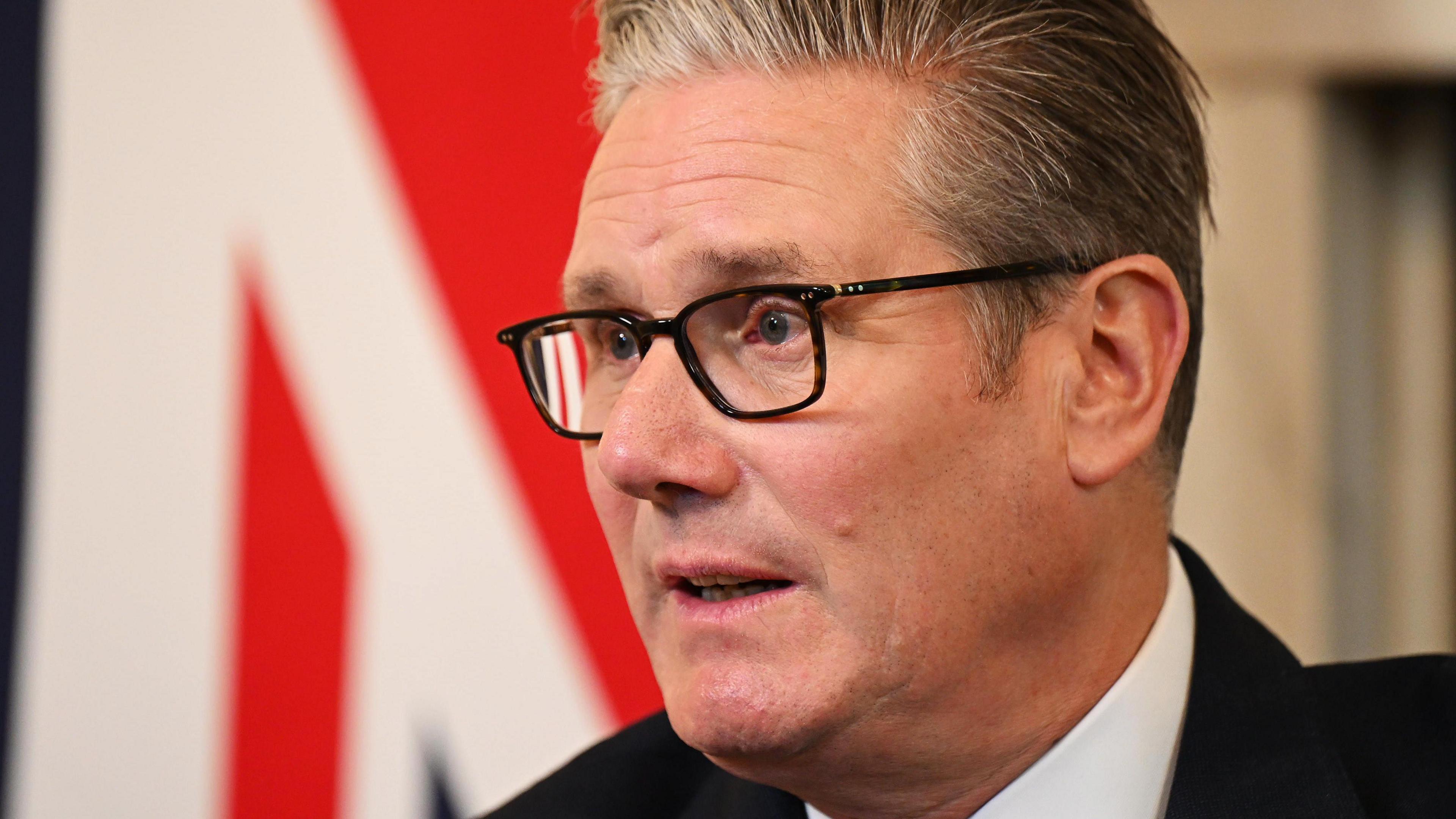 Prime Minister Sir Keir Starmer wears black glasses and a dark suit.
