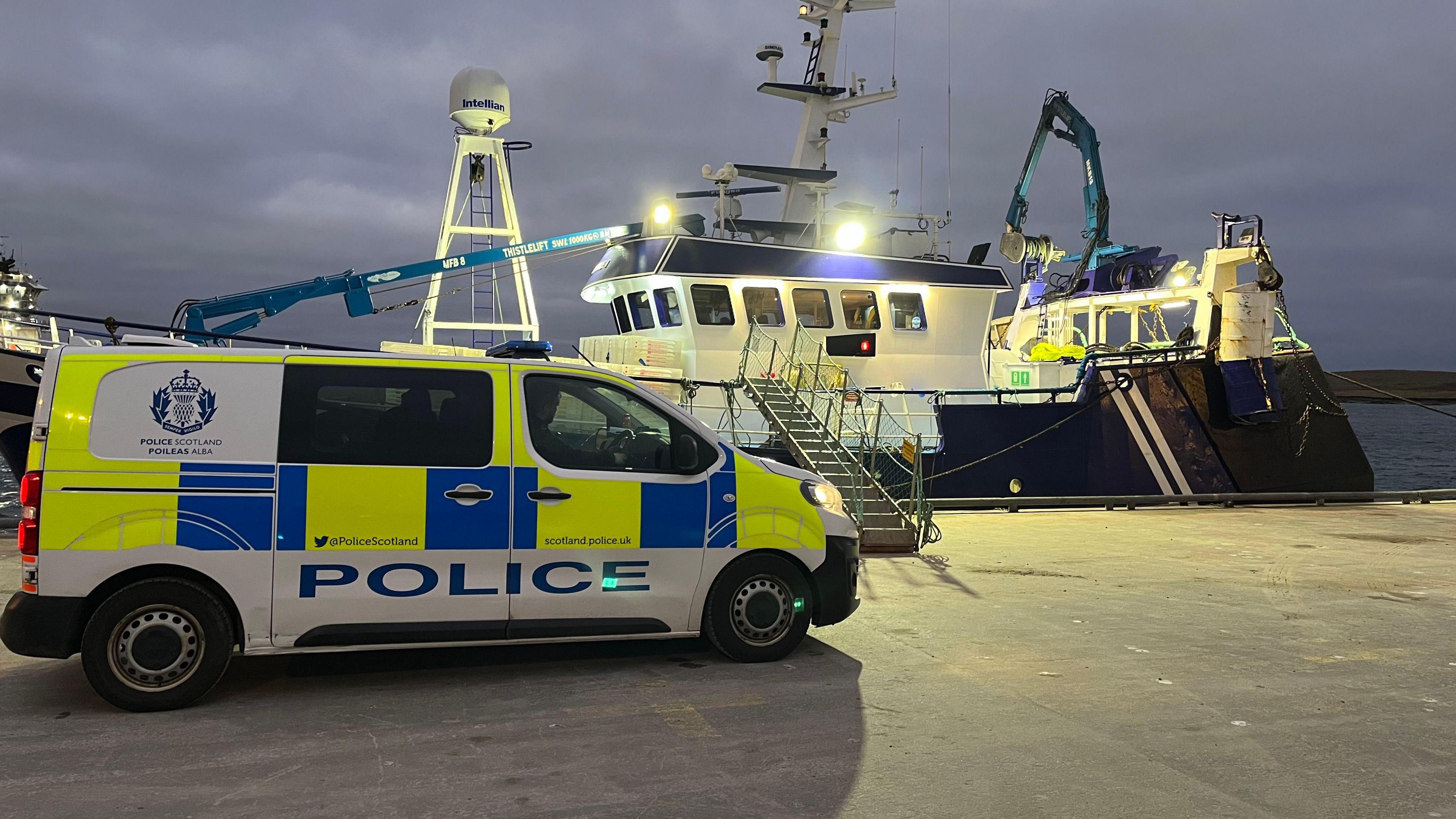 the plane was found by this fishing boat. a police car is parked on the road infront of the fishing boat, whch is still in the water. 