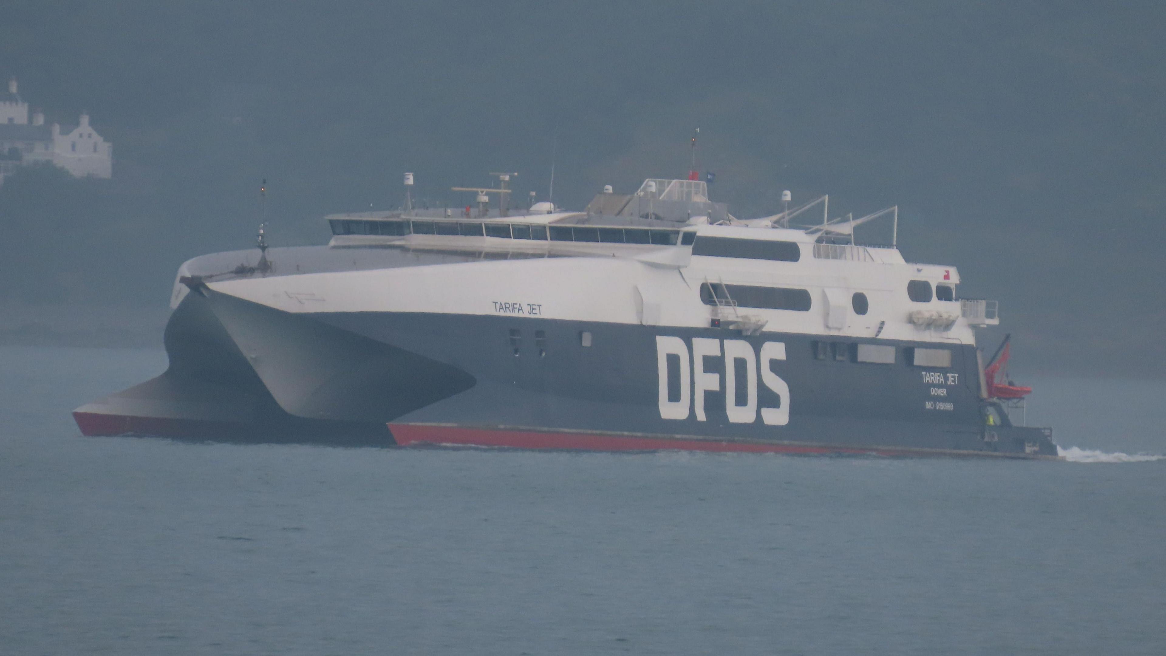 DFDS' Tarifa Jet vessel on the water in Jersey. It is half dark blue and half white. It has DFDS written in large white capital letters on the bottom half of the boat.