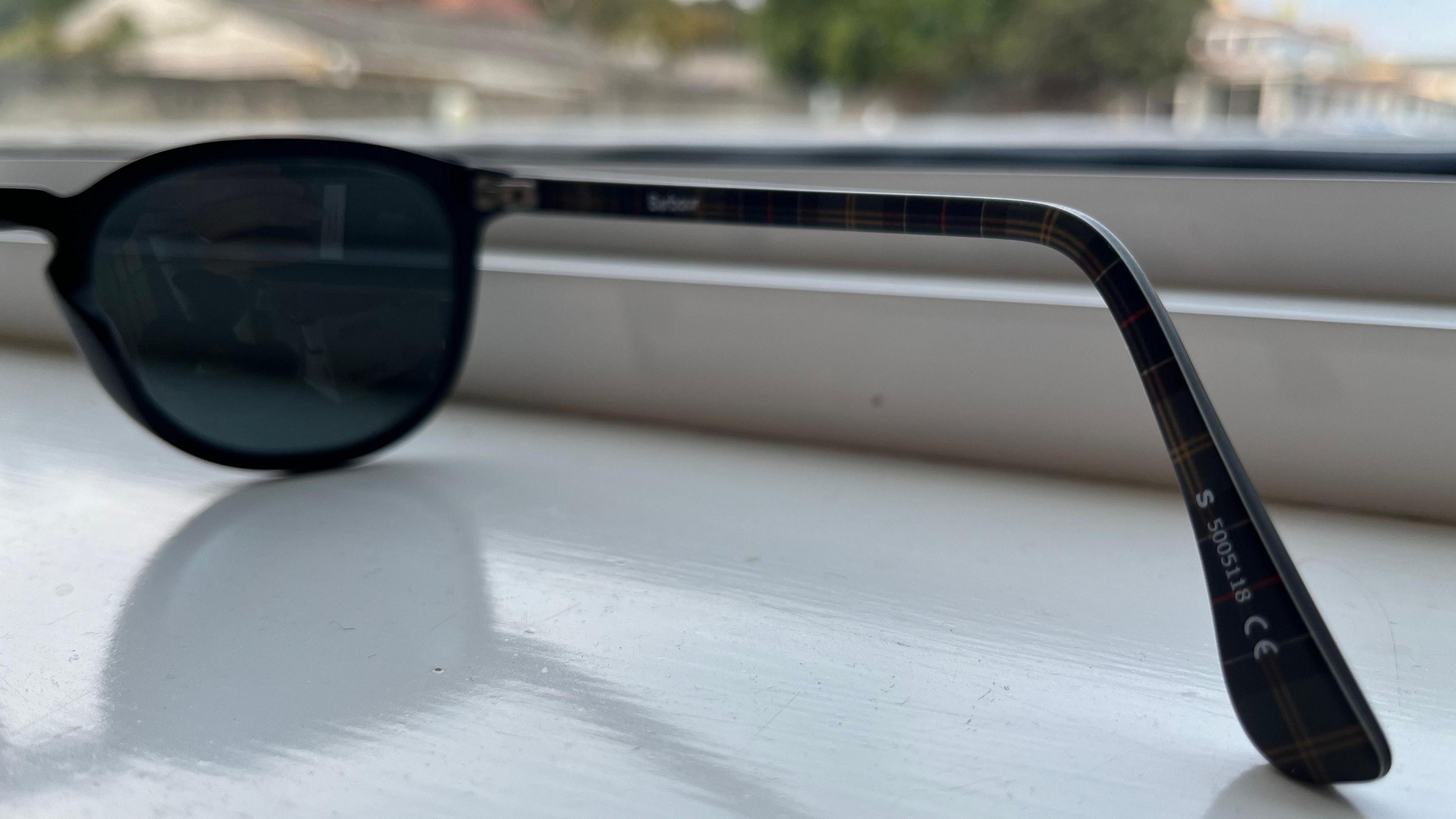 A pair of black sunglasses on a windowsill with European standard for UV protection symbol.