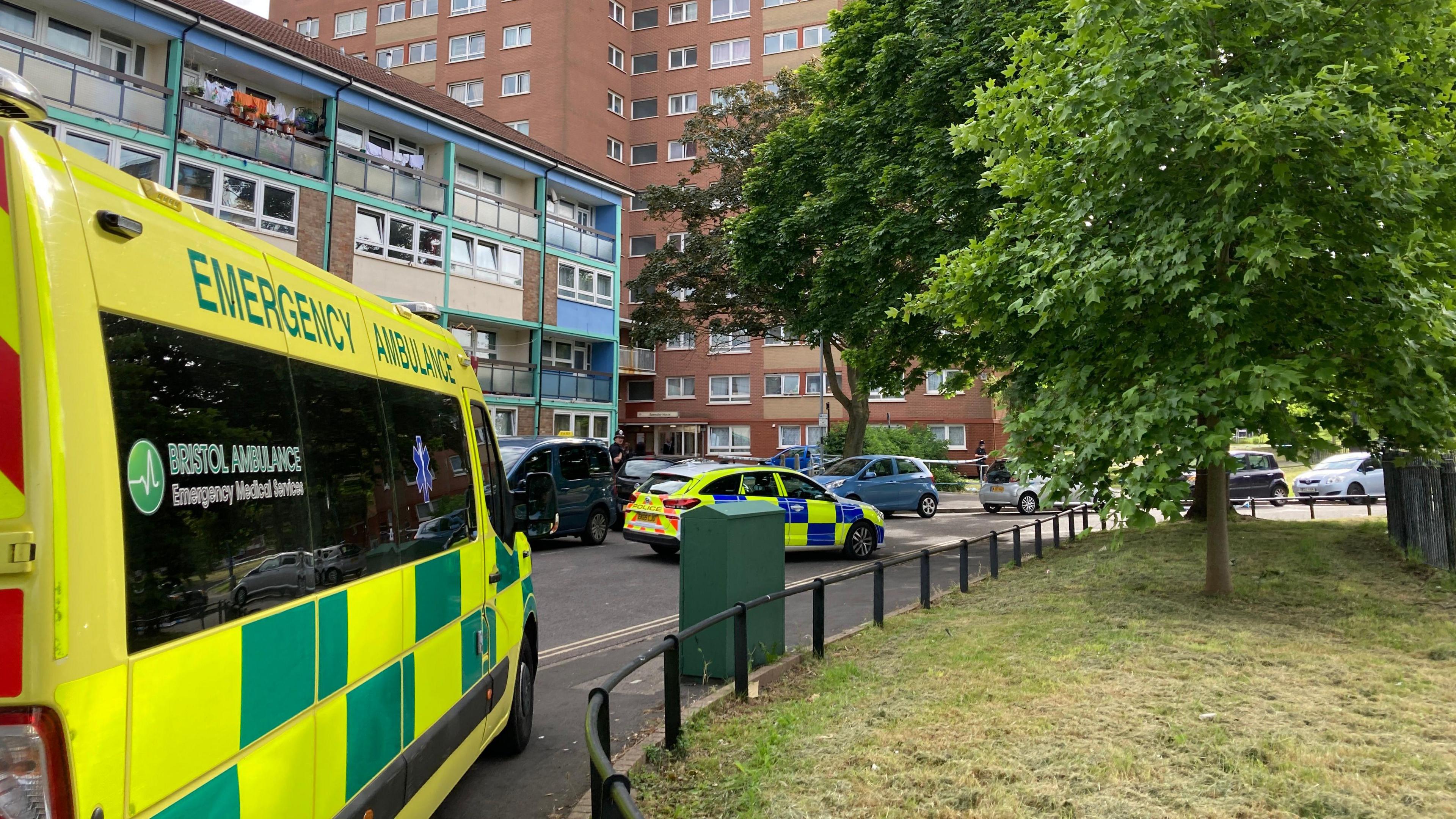 Ambulance to the left, with a police car in front of residential block of flats