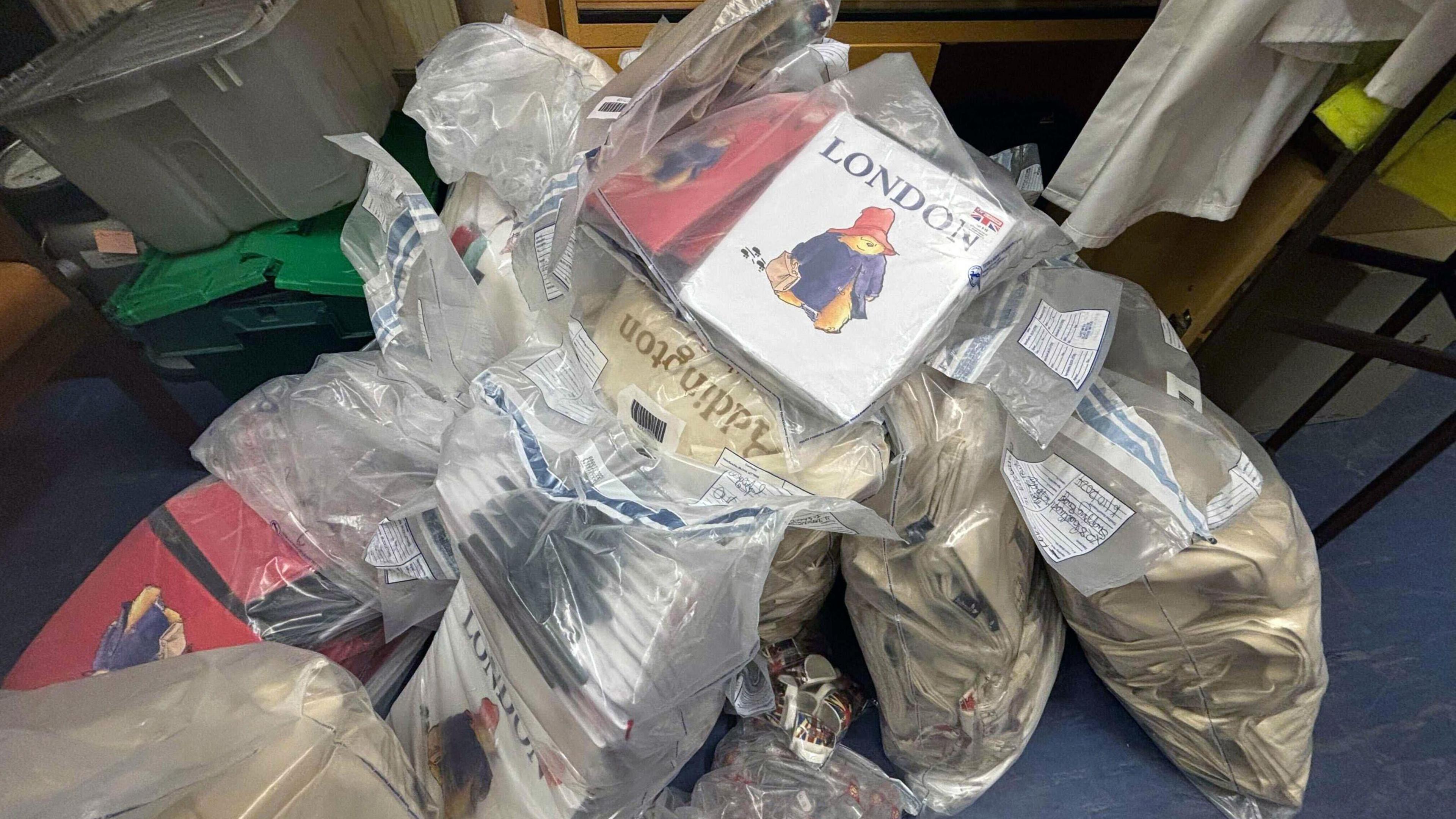 Piles of see through bags holding white, red and cream books and bags with the words 'Paddington' and 'London' on them and images of Paddington Bear in a blue duffle coat and red hat