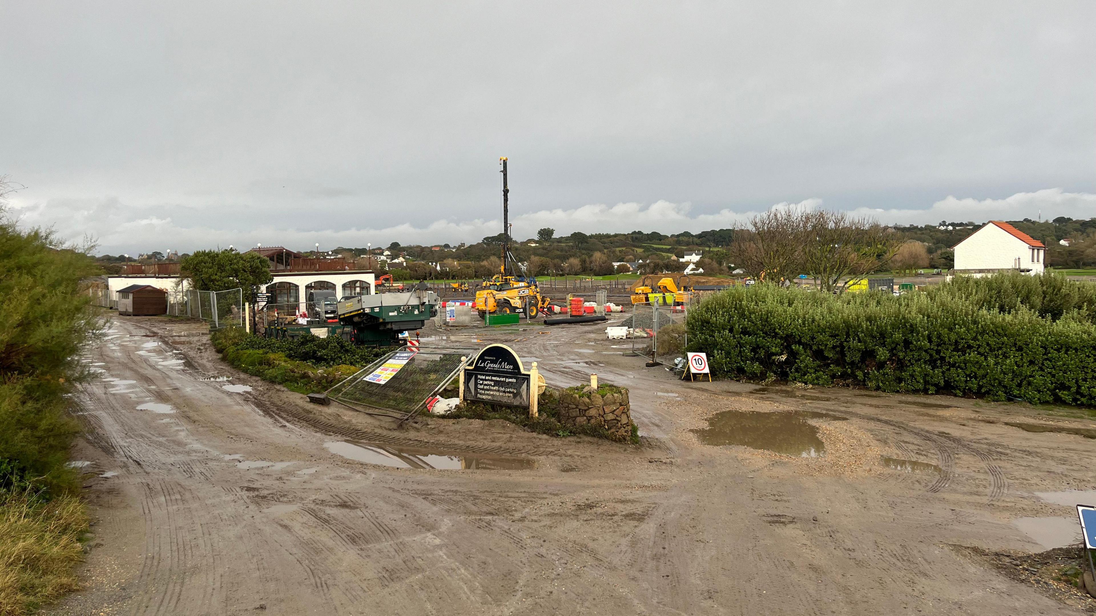 A muddy building site with a large yellow drilling pylon in the background. 