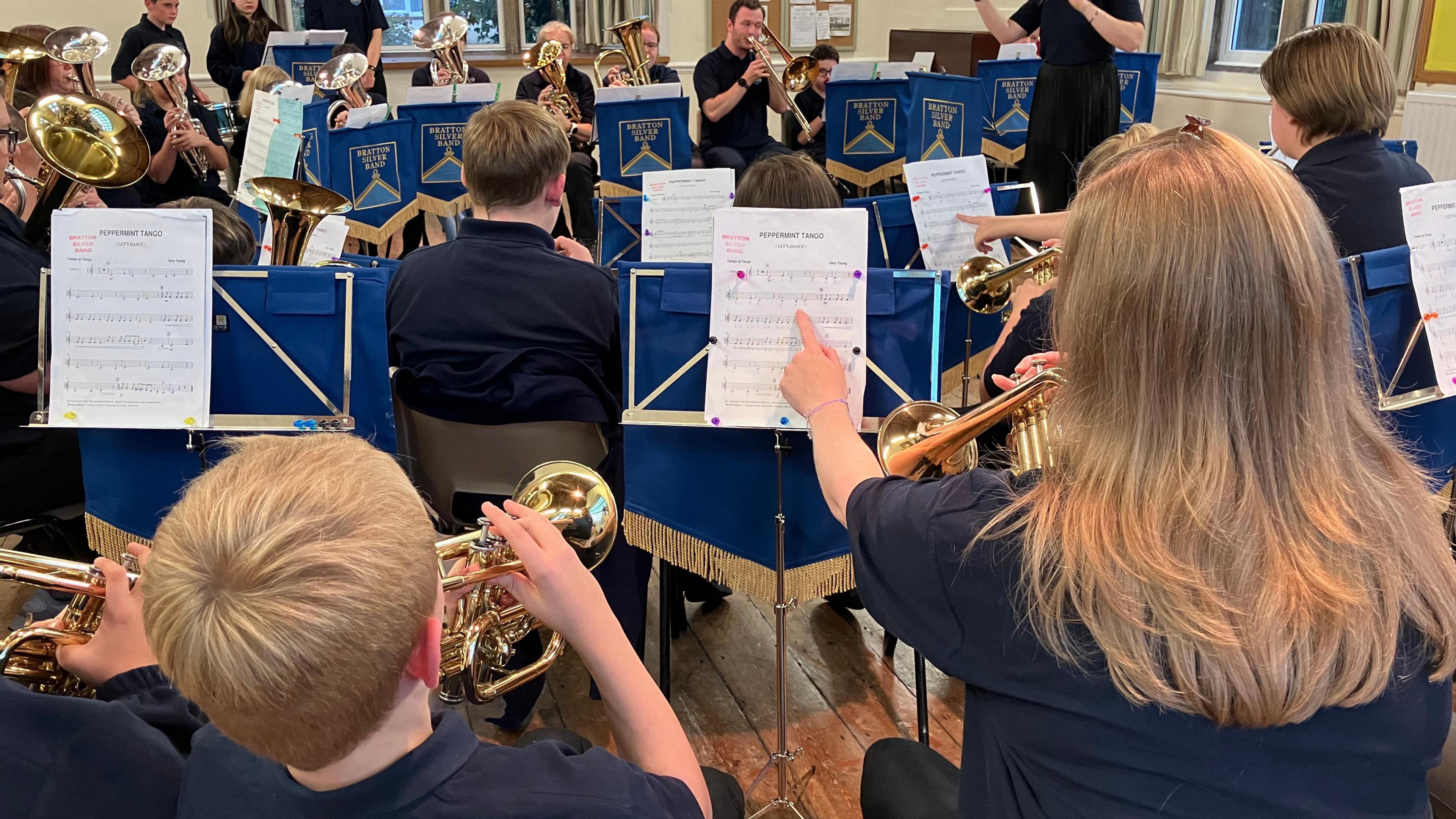 Pupils are playing their brass instruments while reading from sheet music. 