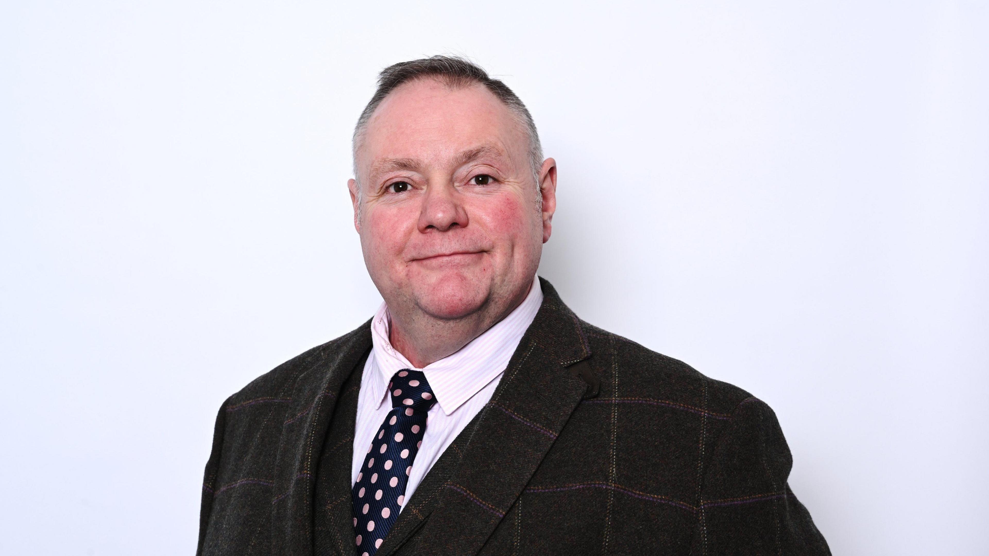 Council leader Stephen Simkins, wearing a brown check suit and tie standing against a white background