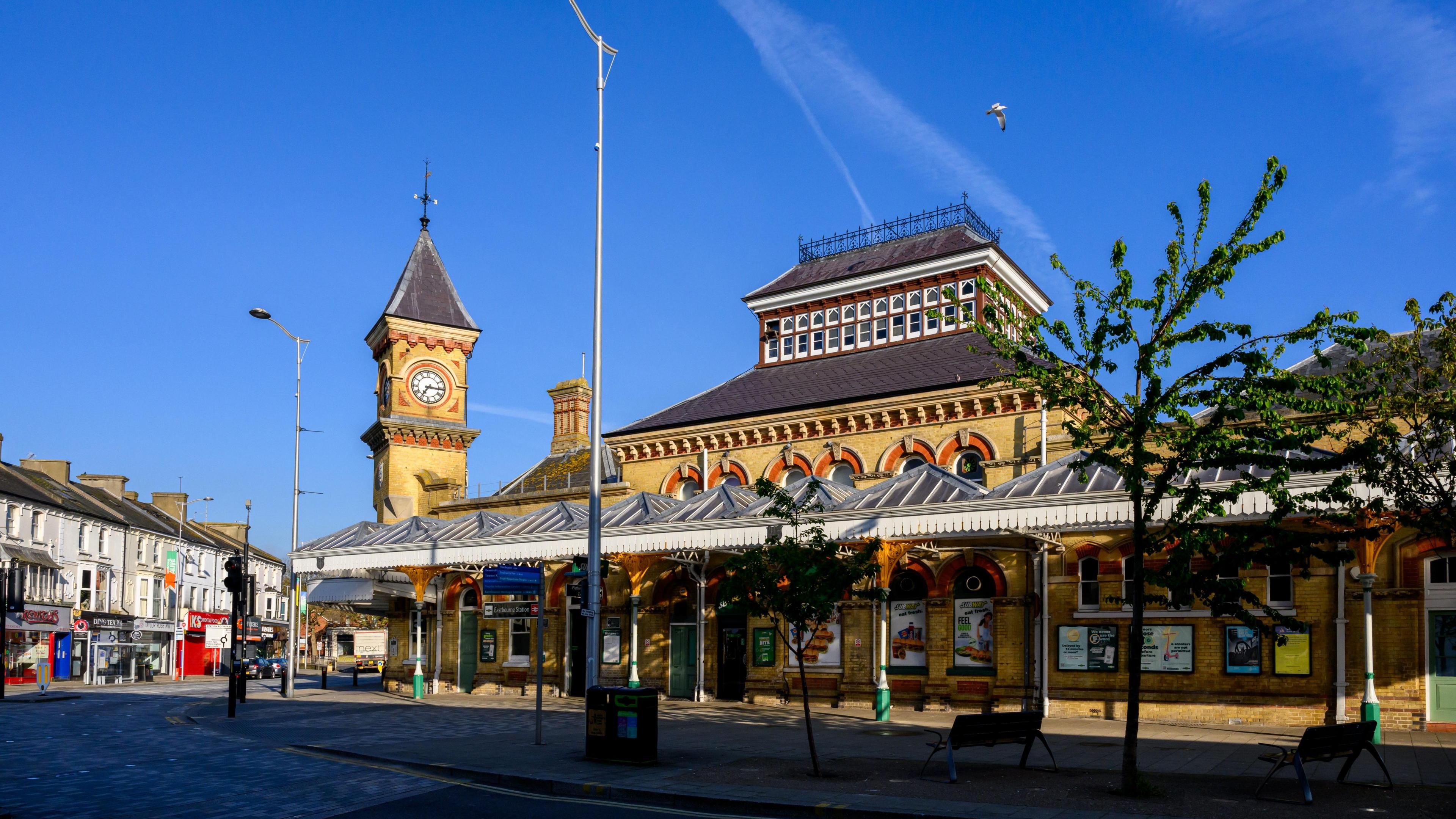 Eastbourne railway station, a yellow brick Victorian Gothic building with a pagoda-style roof and a clock tower, and a portico held up with metal columns at its front.