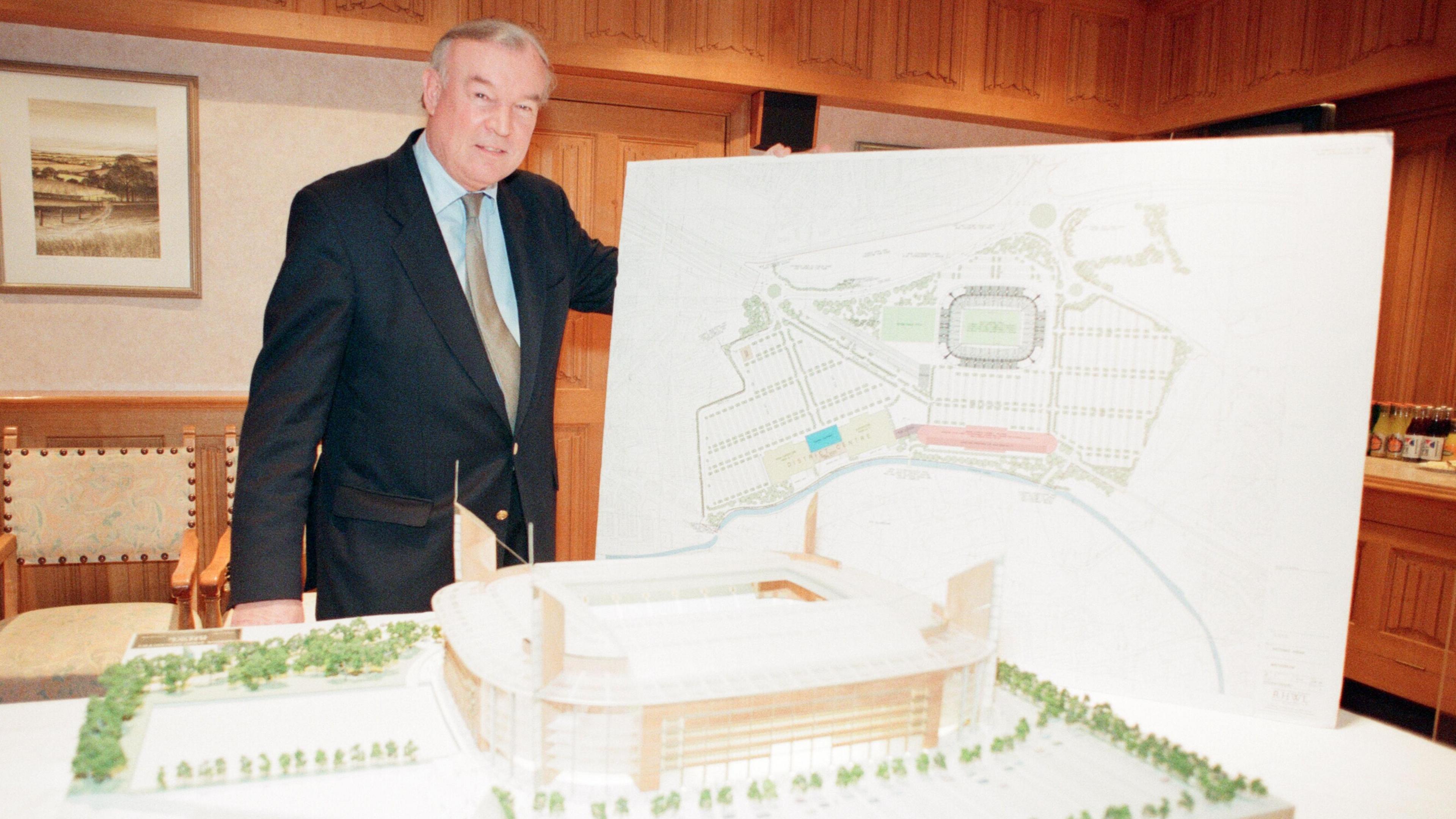 Former Coventry City Chairman Bryan Richardson shows plans and a model for 'Arena 2000' in the boardroom of Highfield Road in 1997. The boardroom has a wood panelling. Bryan is wearing a suit and tie There is a model of the planned stadium on the table in front of him.