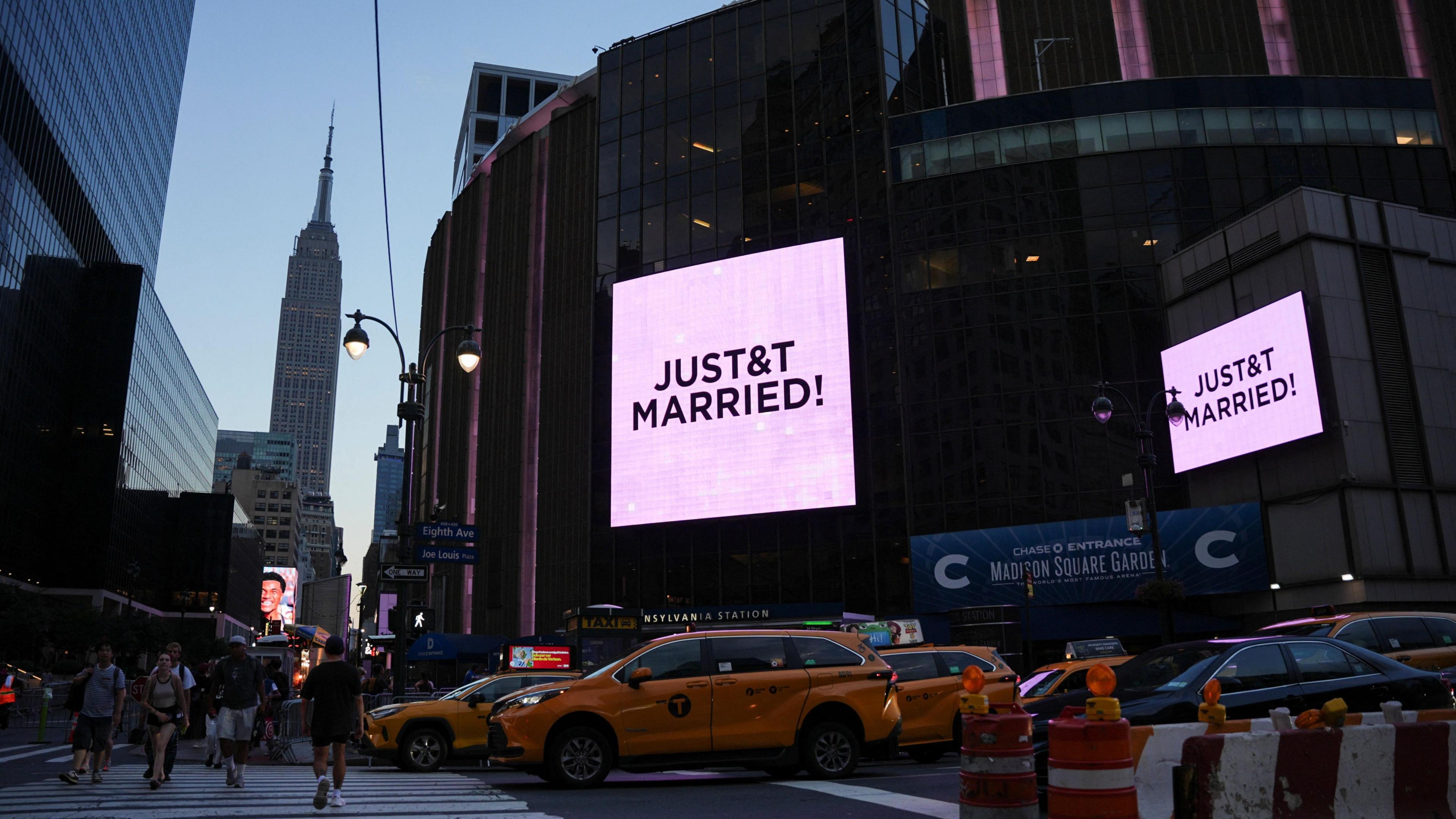 Pink screens outside Madison Square Garden showing New York in the twilight, with Empire State Building in the background and yellow taxis in the foreground