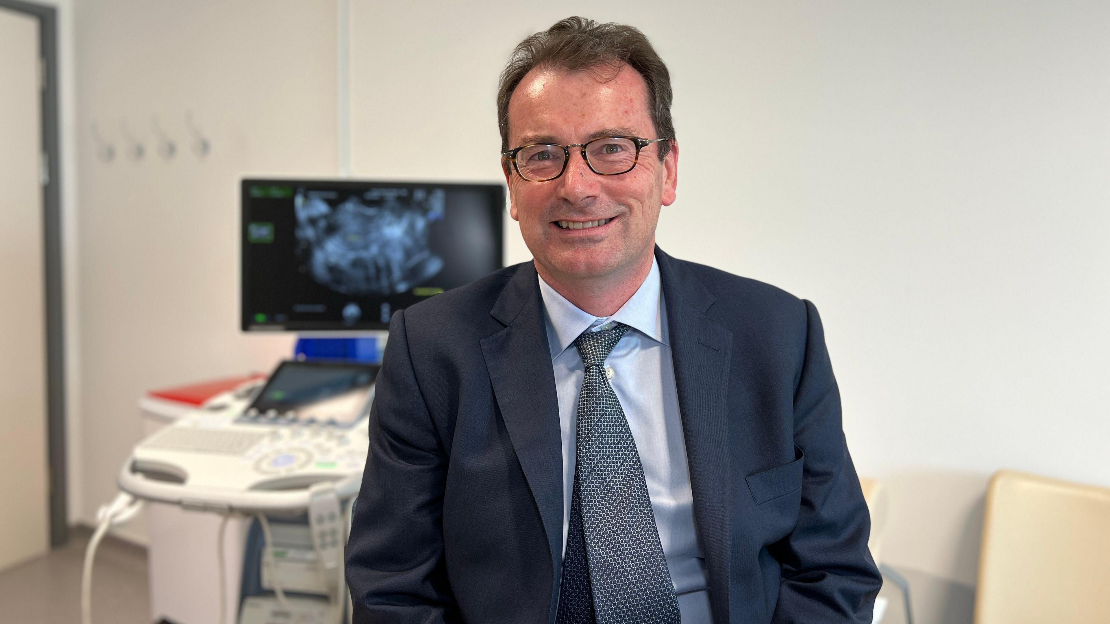 Prof Enda McVeigh smiles at the camera with a baby scanner behind him