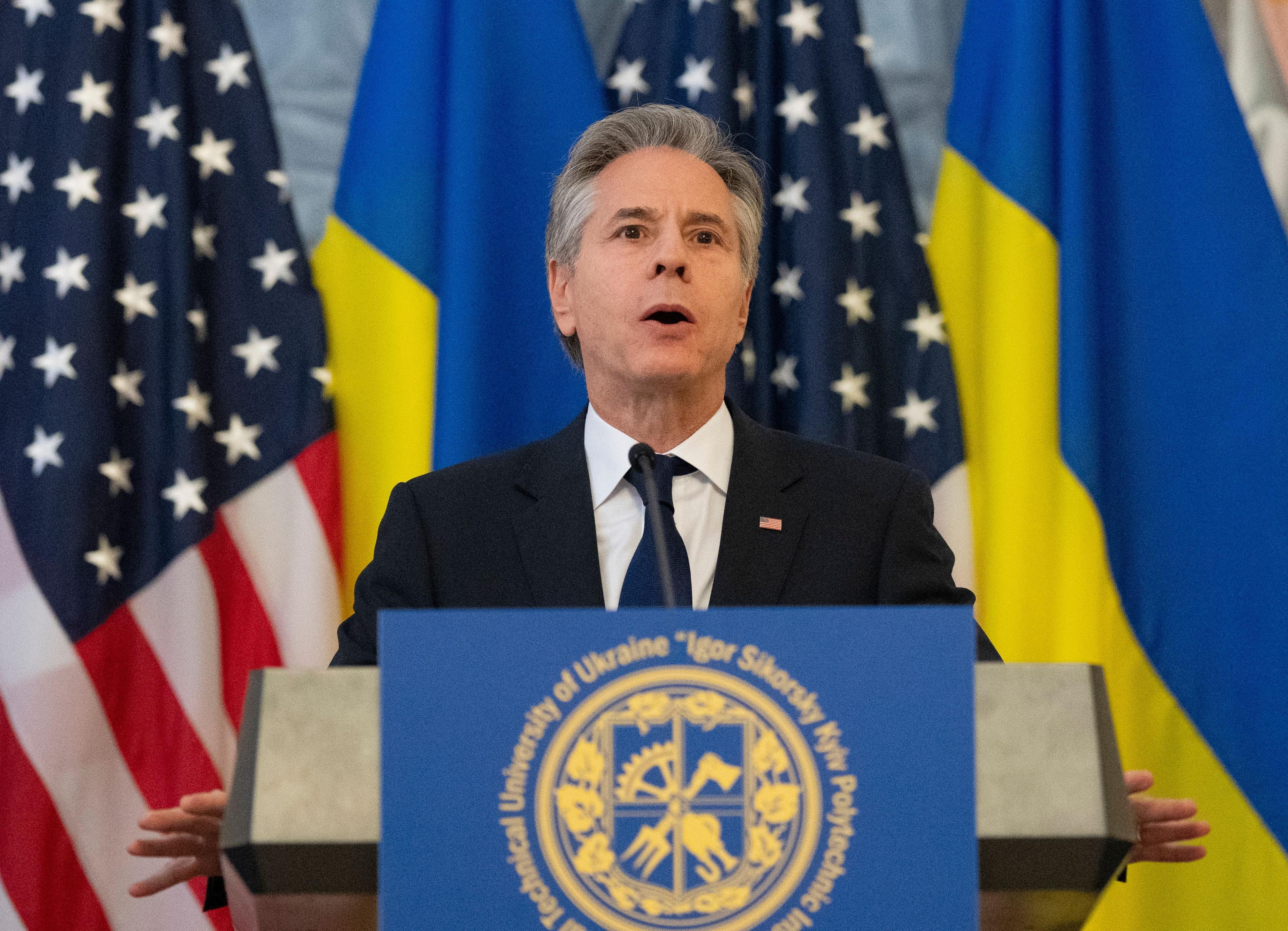 Antony Blinken standing behind a podium with US and Ukranian flags in the background