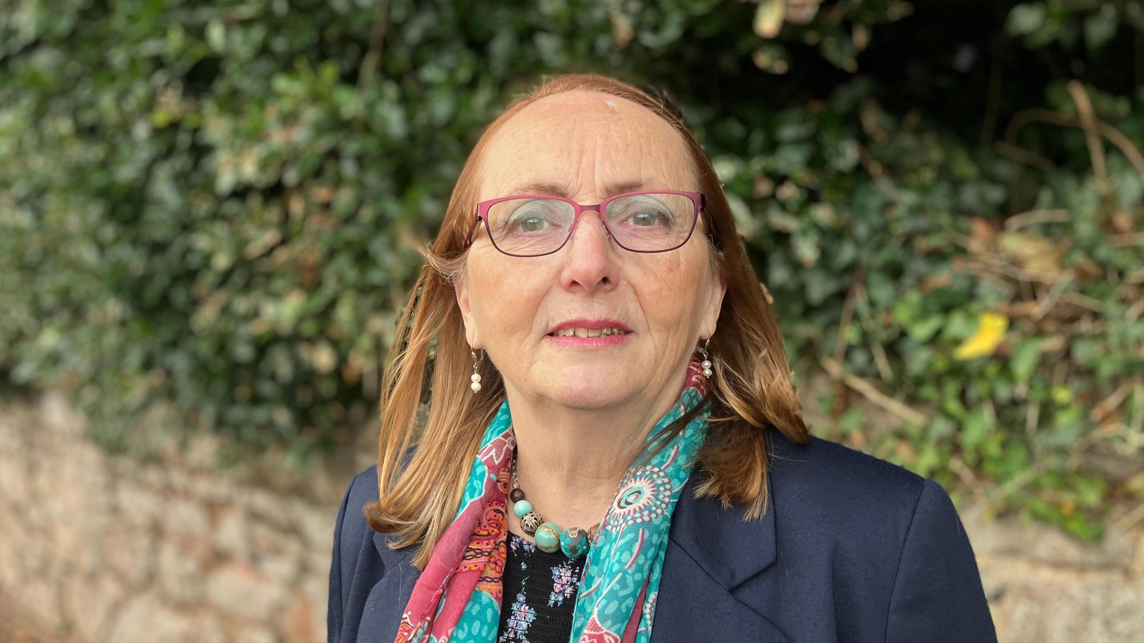 A woman stands in a street in Torquay, there is a stone wall in the background with greenery above it. 