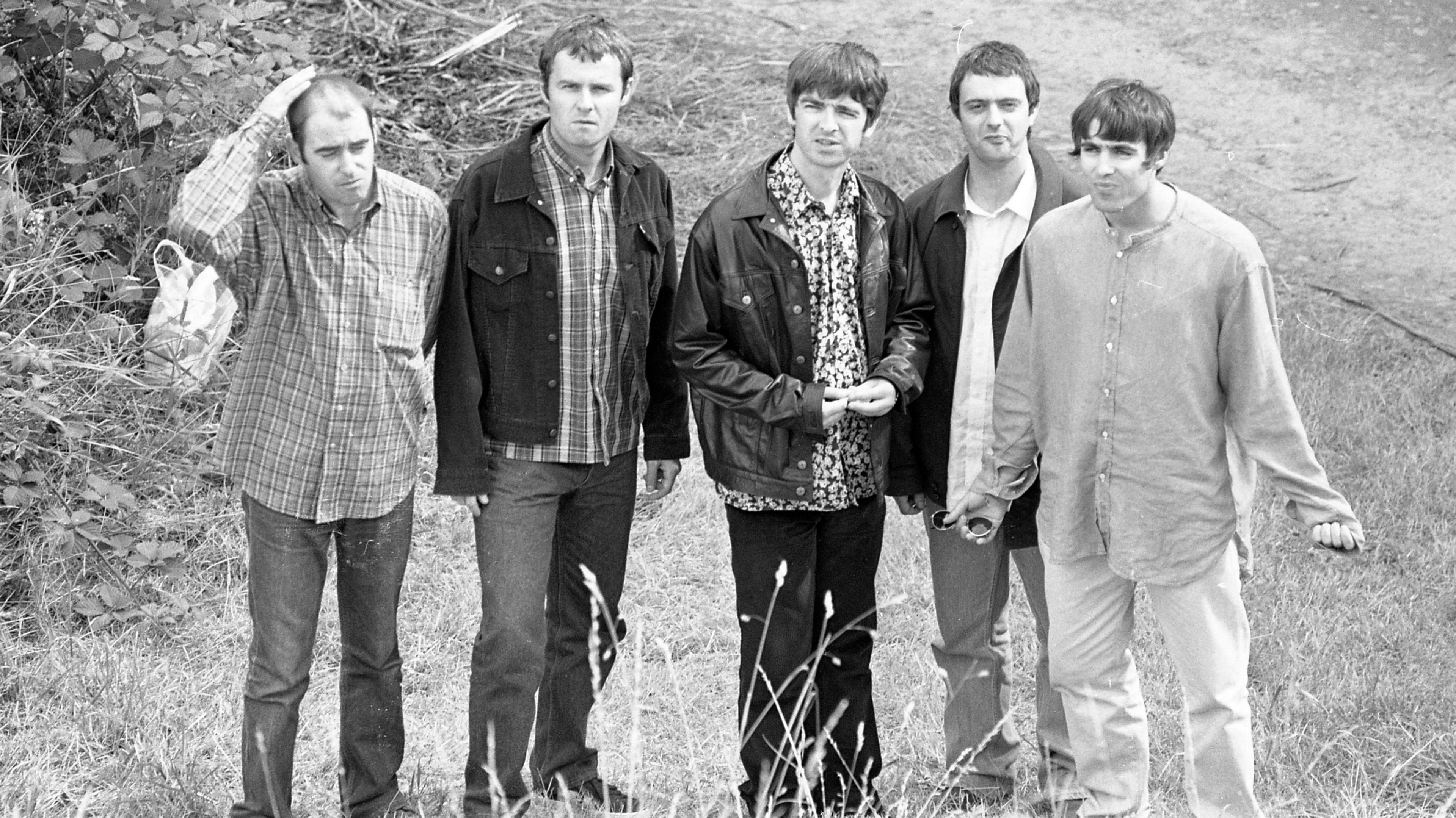 Black and white photo of five men, two being Liam and Noel Gallagher of Oasis. They are standing in a field at Slane Castle.