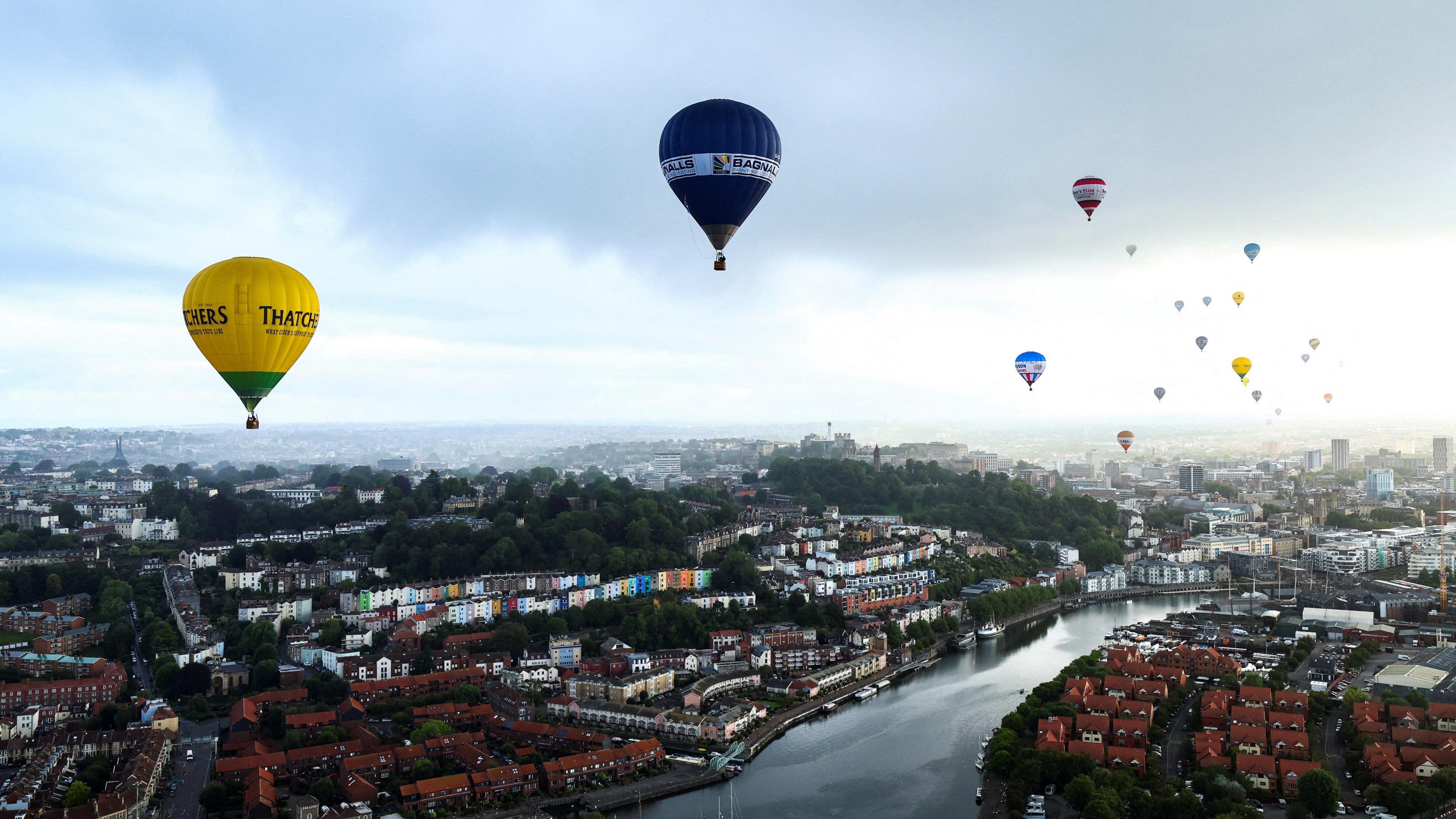 A wide shot image showing many hot air balloons flying over Bristol. The city landscape can be seen in the distance.