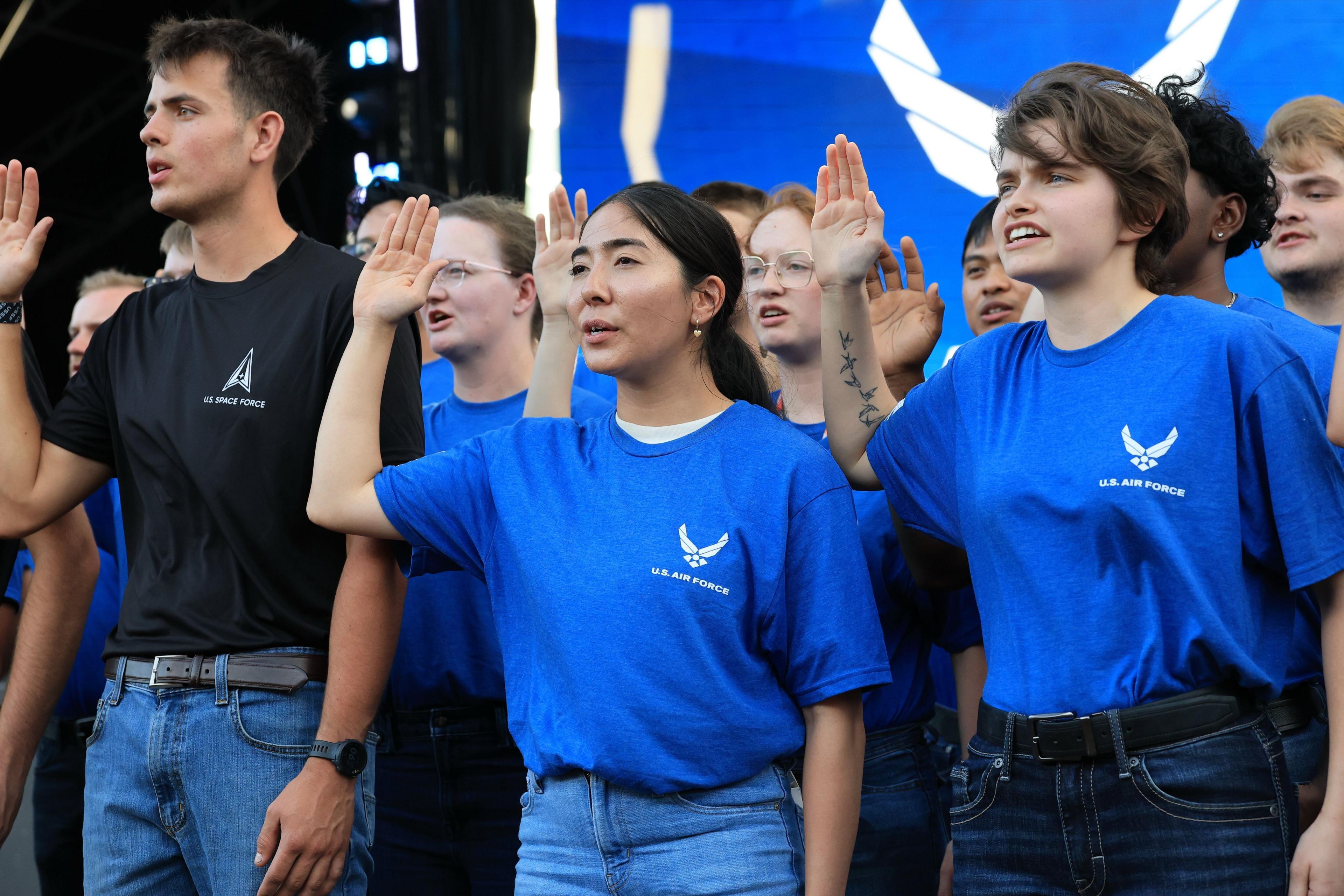 A ling of young people in blue and black Space Force logo t-shirts hold up their right hand as they take an oath