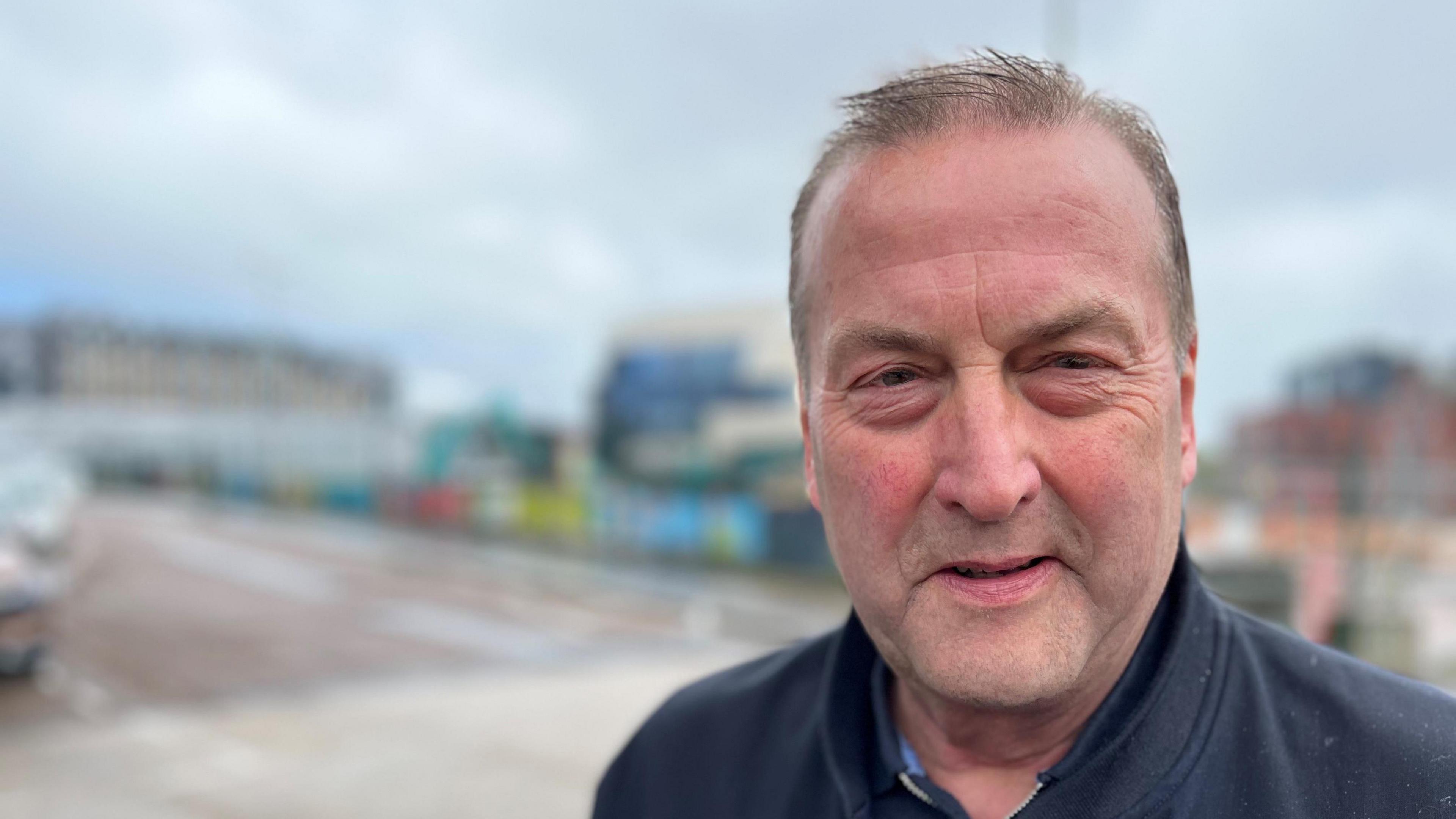 Exeter City Council leader Phil Bialyk wearing a blue top and jacket with a blurred city background