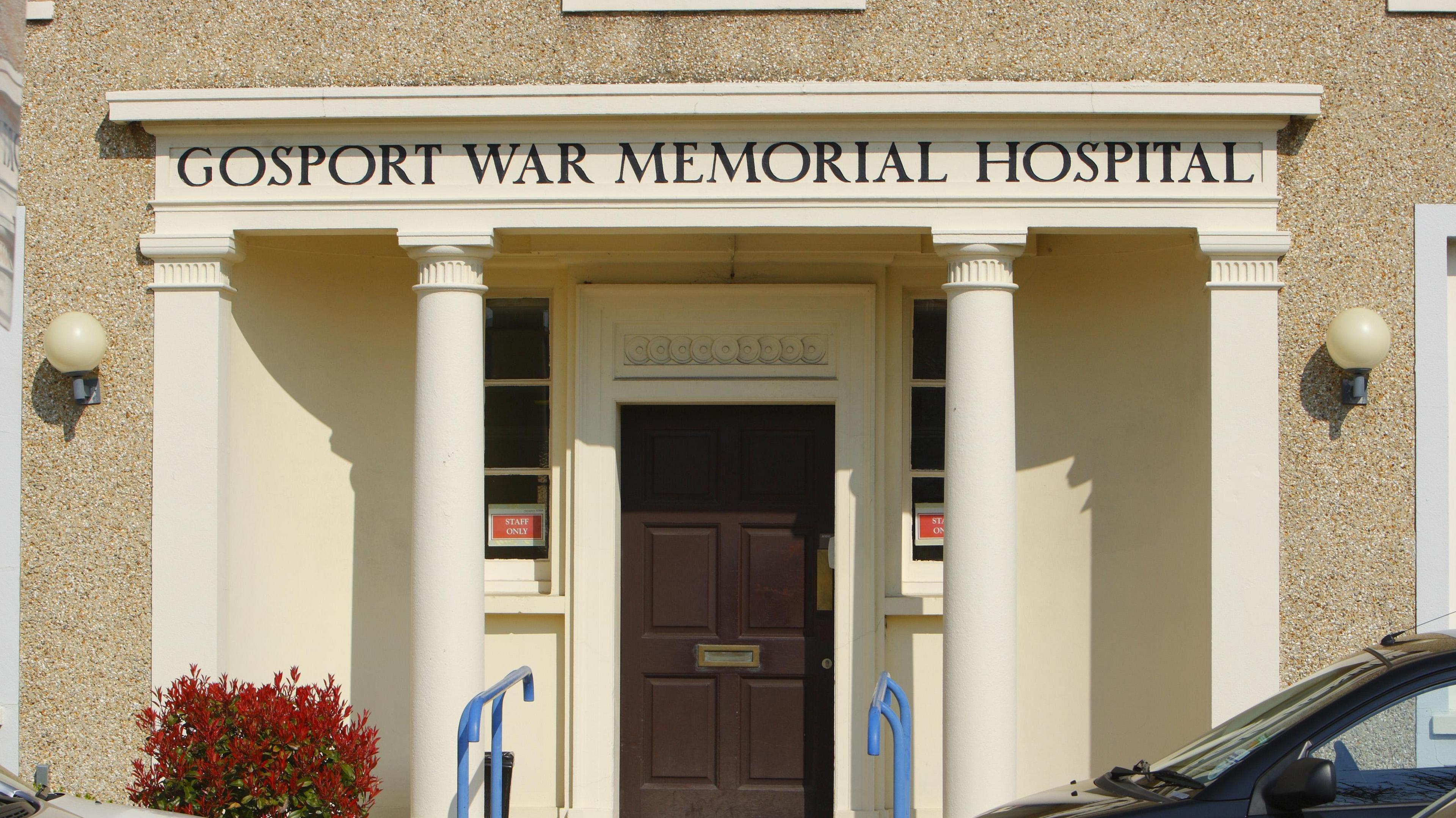 The front façade of Gosport War Memorial Hospital. It has four white pillars, with the hospital's name in black letters above them.