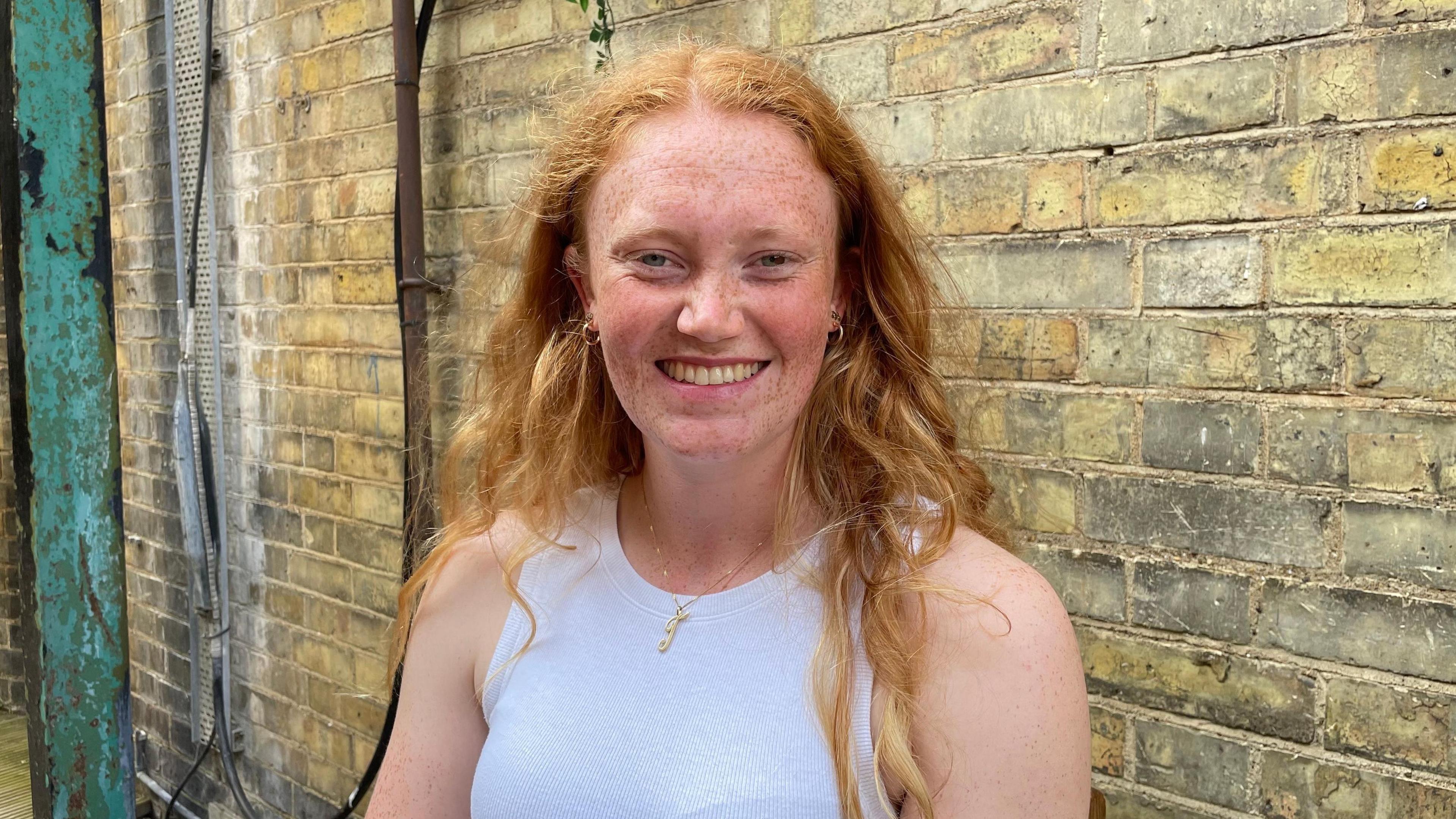 A woman, Tanya Sargeant, is stood in front of a brick wall. She's smiling and wearing a white top